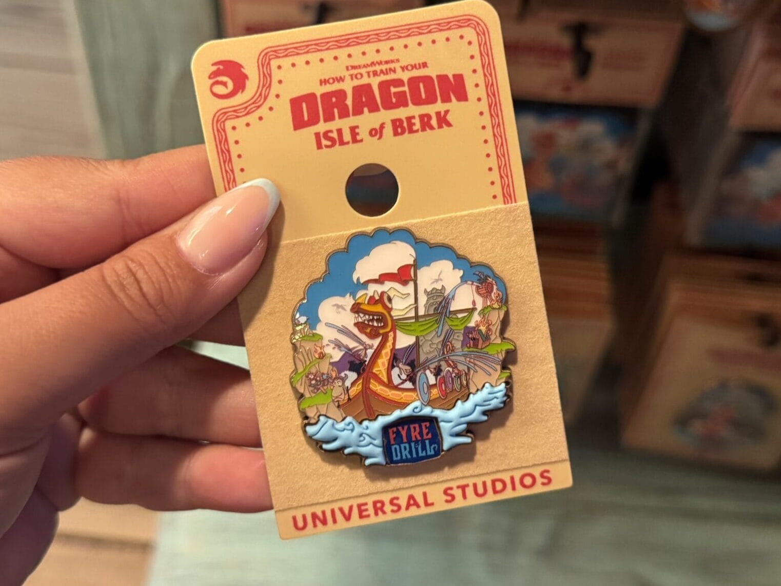 A hand displays a "How to Train Your Dragon" Isle of Berk merch pin from Universal Studios, not Disney like Cinderella Castle.