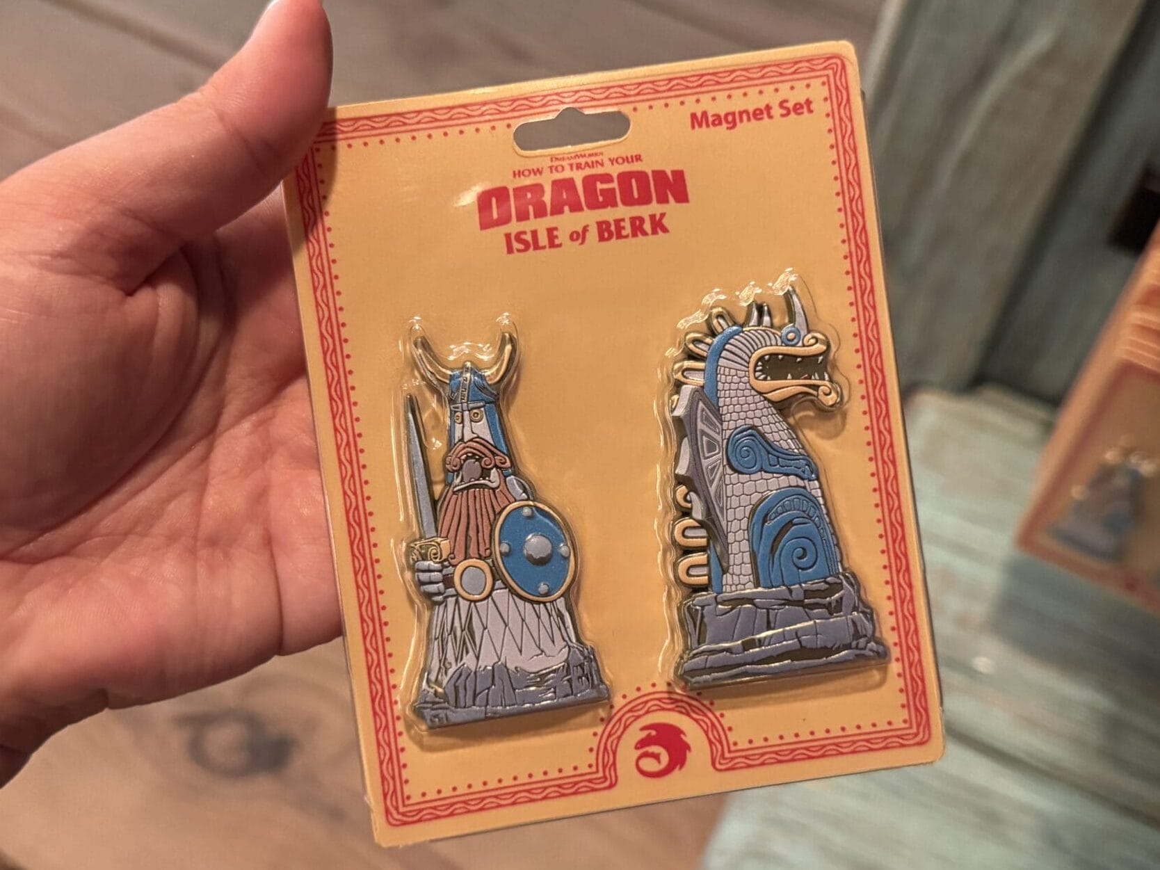 A hand holds a How to Train Your Dragon Isle of Berk magnet set with Viking and Spit Fyre ships, unlike any Disney castle merch.