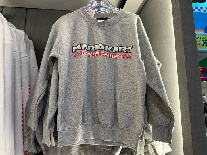 Gray sweatshirt on a rack with "Mario Kart Bowser’s Challenge" logo—Nintendo vibes, not like classic Disney castle apparel.