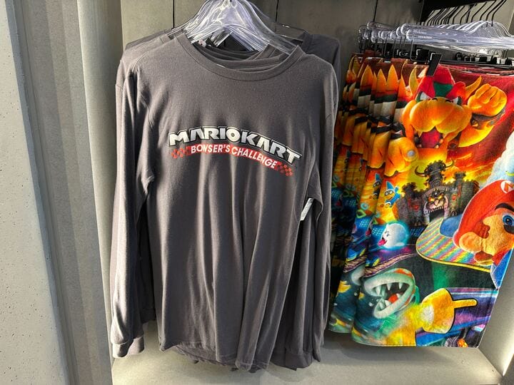 A gray long-sleeve "Mario Kart: Bowser's Challenge" shirt among Epic Universe Mario Motors gear, not Disney castle merchandise.