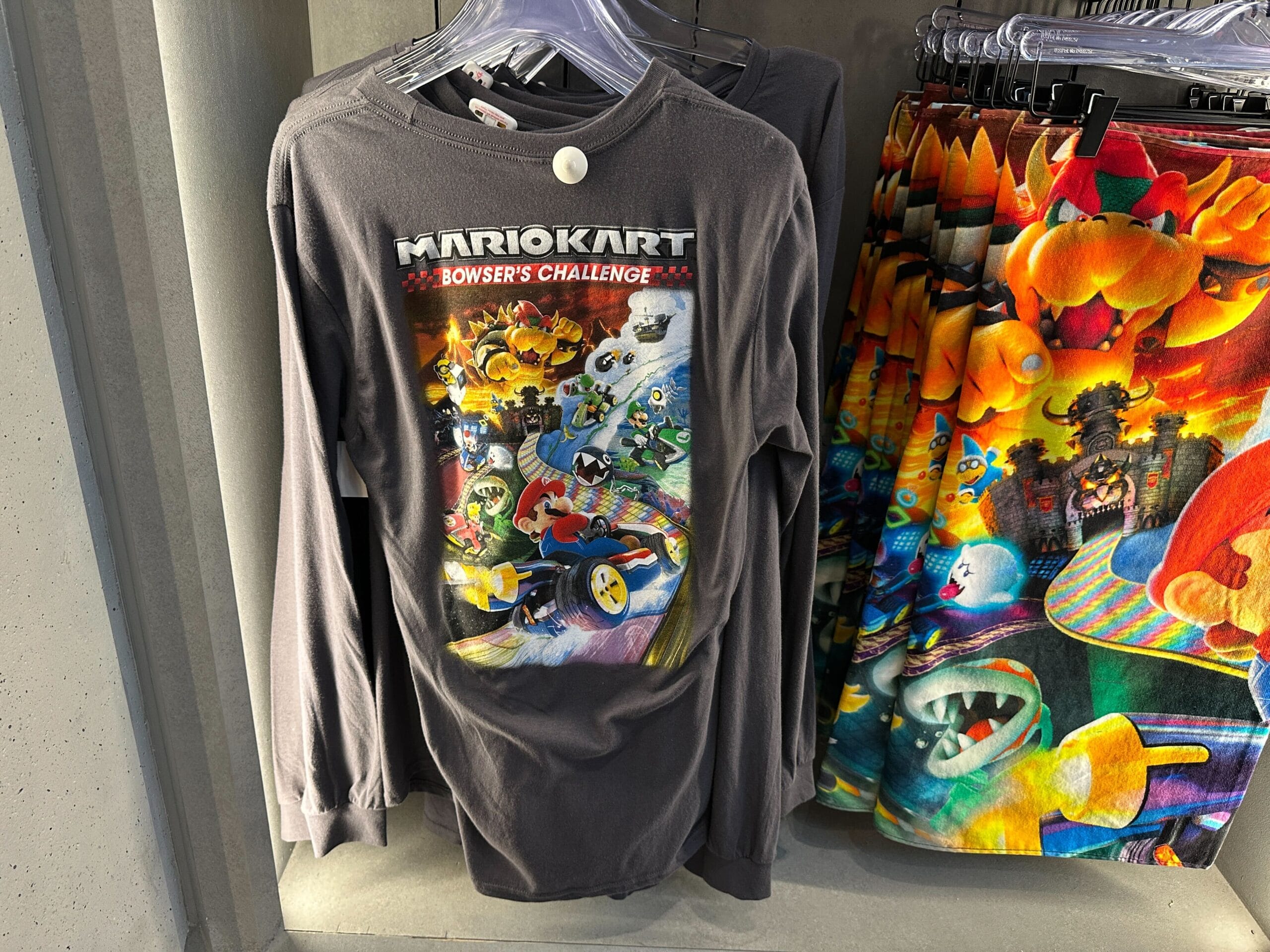 Long-sleeve Mario Kart: Bowser’s Challenge shirt and Super Nintendo World shorts on a rack—much like Disney parks’ themed apparel.