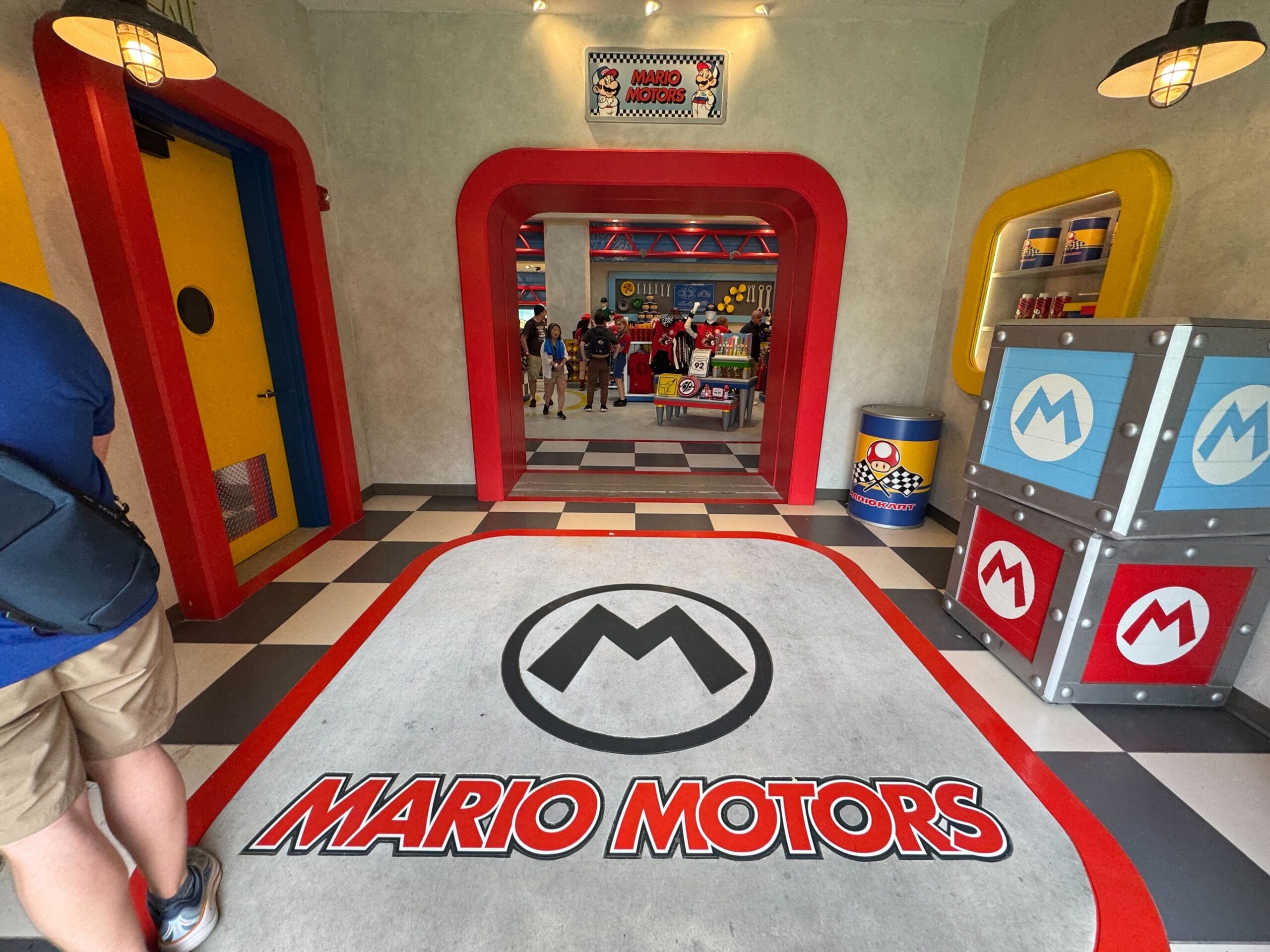 Entrance to Mario Motors, vibrant like Disney park shops, with colorful decor and floor logo, reminiscent of Disney’s immersive lands.