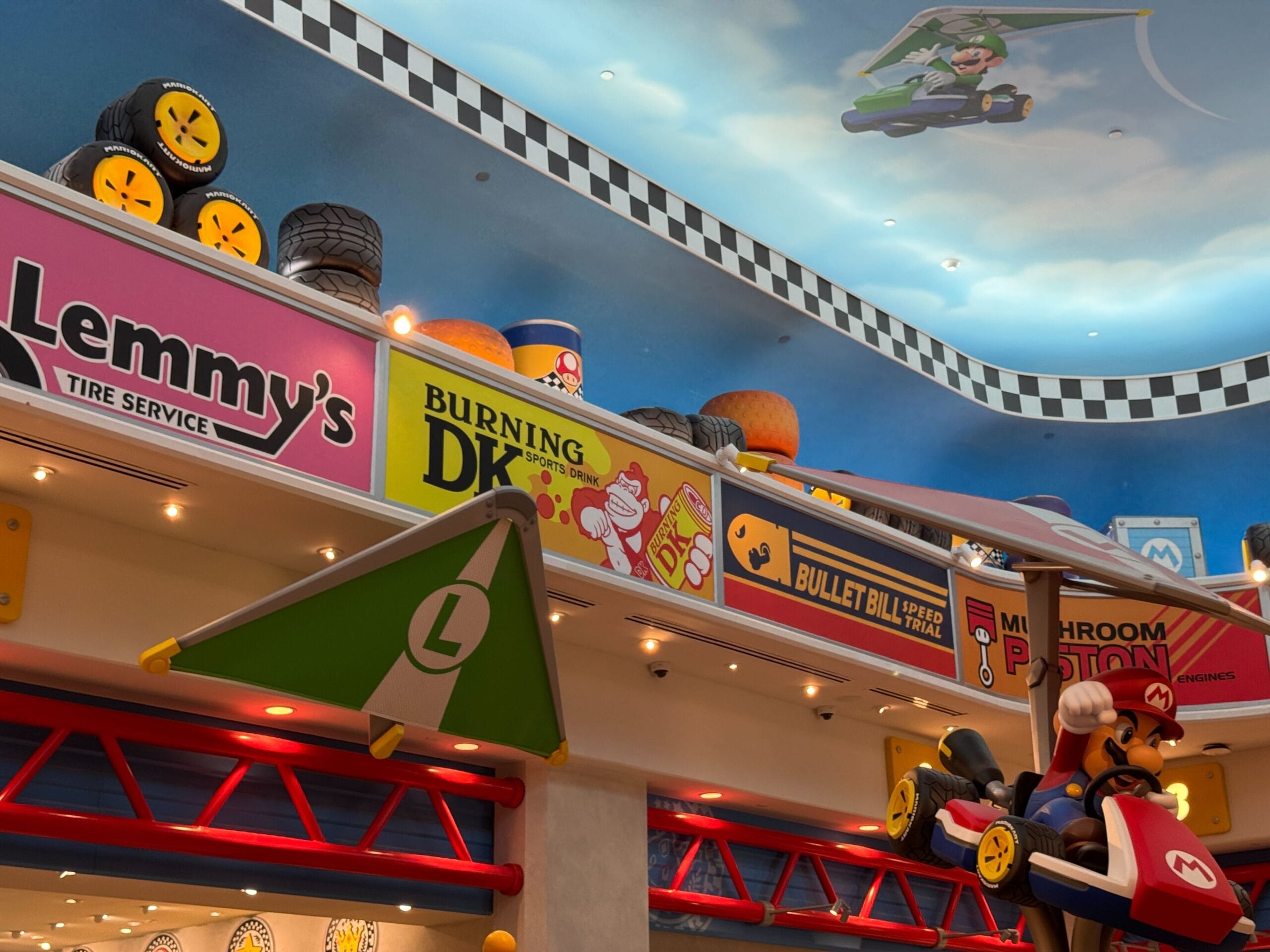 Mario Kart-inspired decor with racing signs, tires, and Mario figure; vibrant like Disney park lands but no castle in this scene.