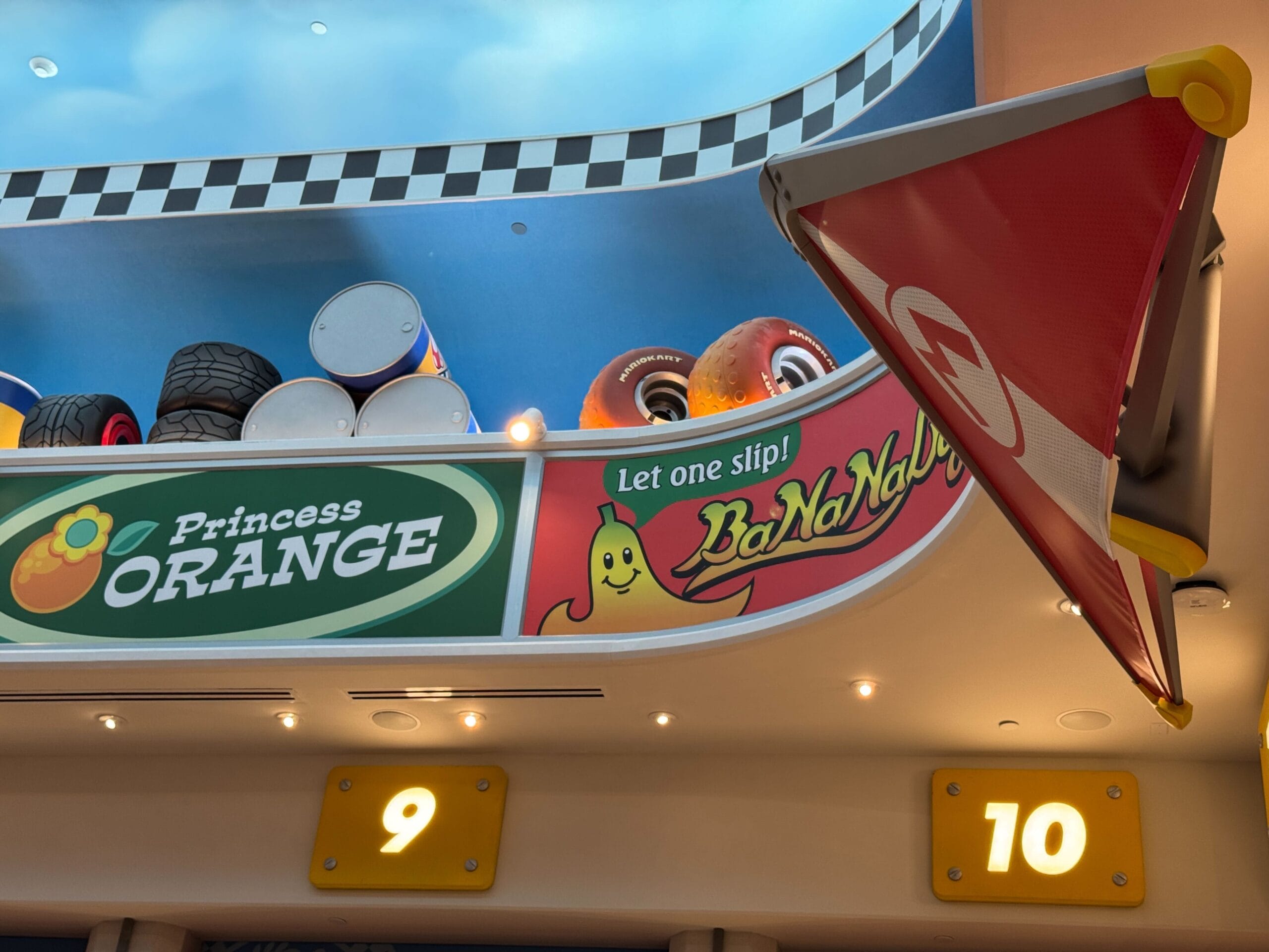 A Mario Kart-themed room featuring playful decor, BaNaNa bar sign, Mario Motors props, and airport-style gates, unlike Disney castles.