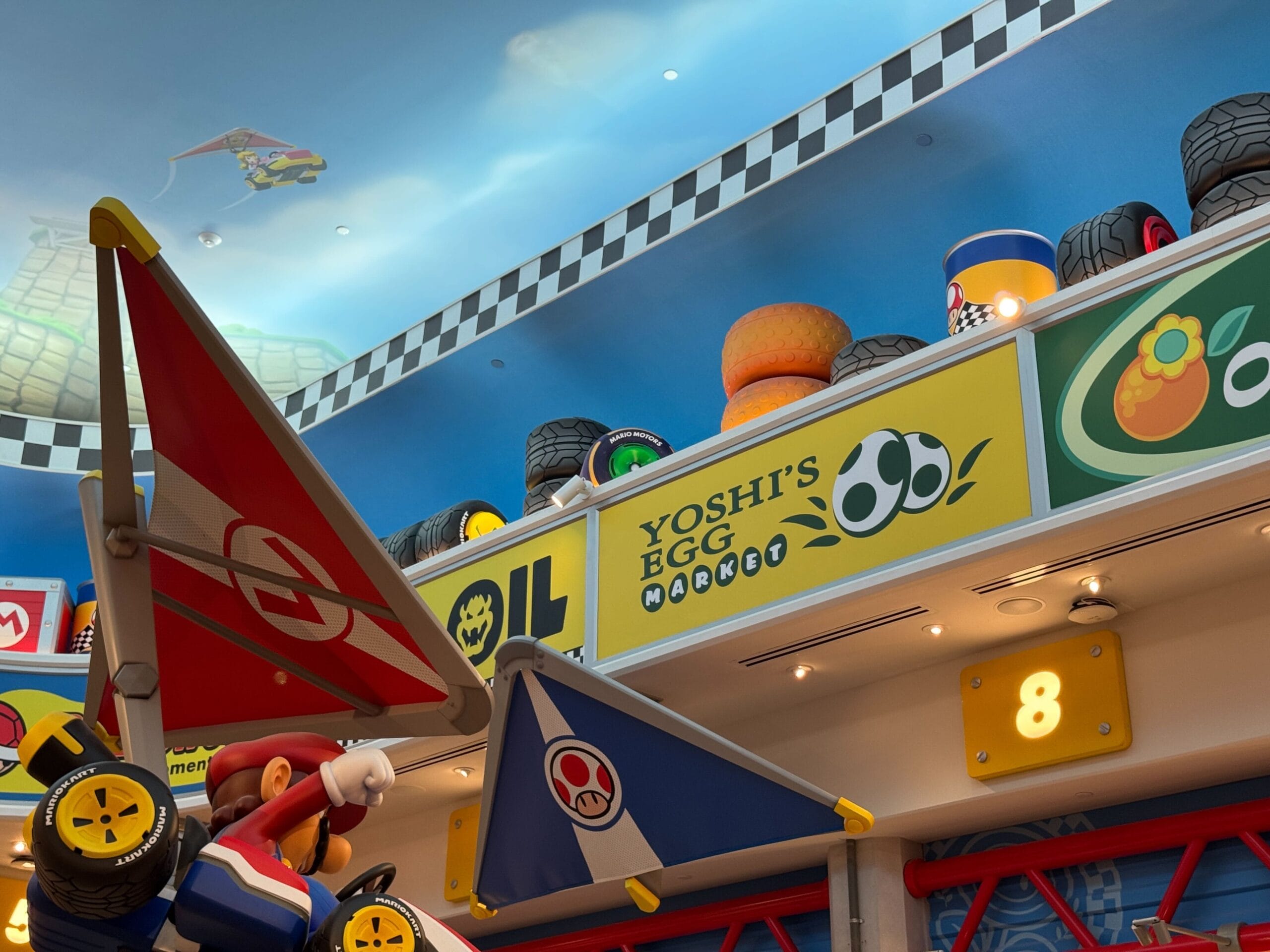 Vibrant indoor area at Super Nintendo World with Mario Kart flags, Mario Motors decor, and Yoshi’s Egg Market sign—distinctly not a Disney castle scene.