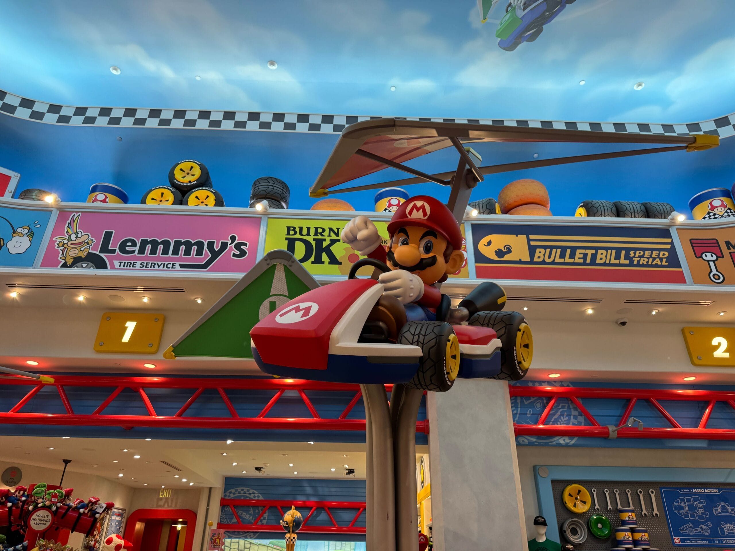 A Mario statue in a red kart with a glider, indoors at Super Nintendo World, with colorful signs, not resembling Disney castles.