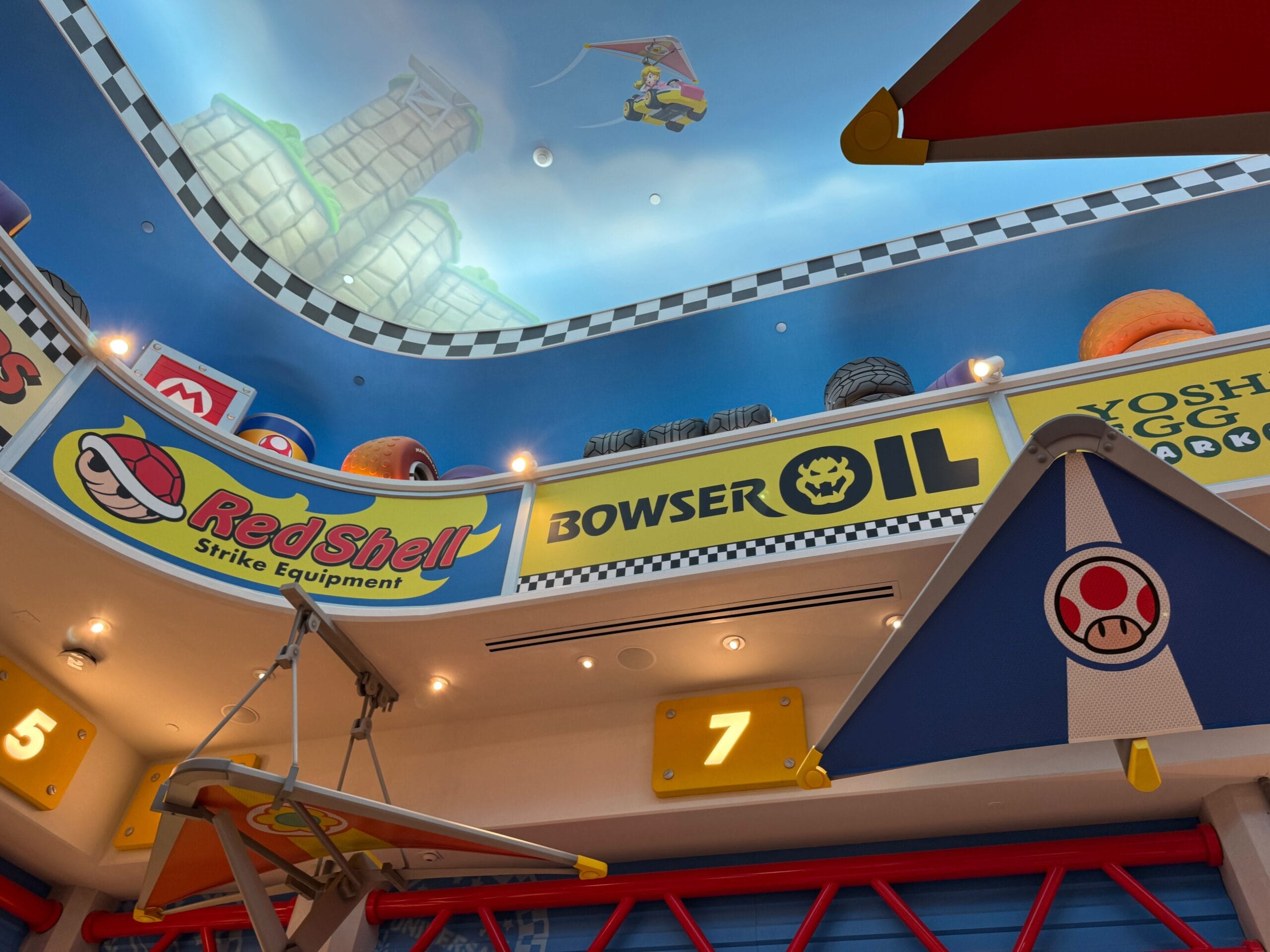 Vibrant Mario Kart-themed interior, Super Nintendo World style, with Bowser Oil and Mario Motors signs beneath a painted sky ceiling—unlike any Disney castle decor.
