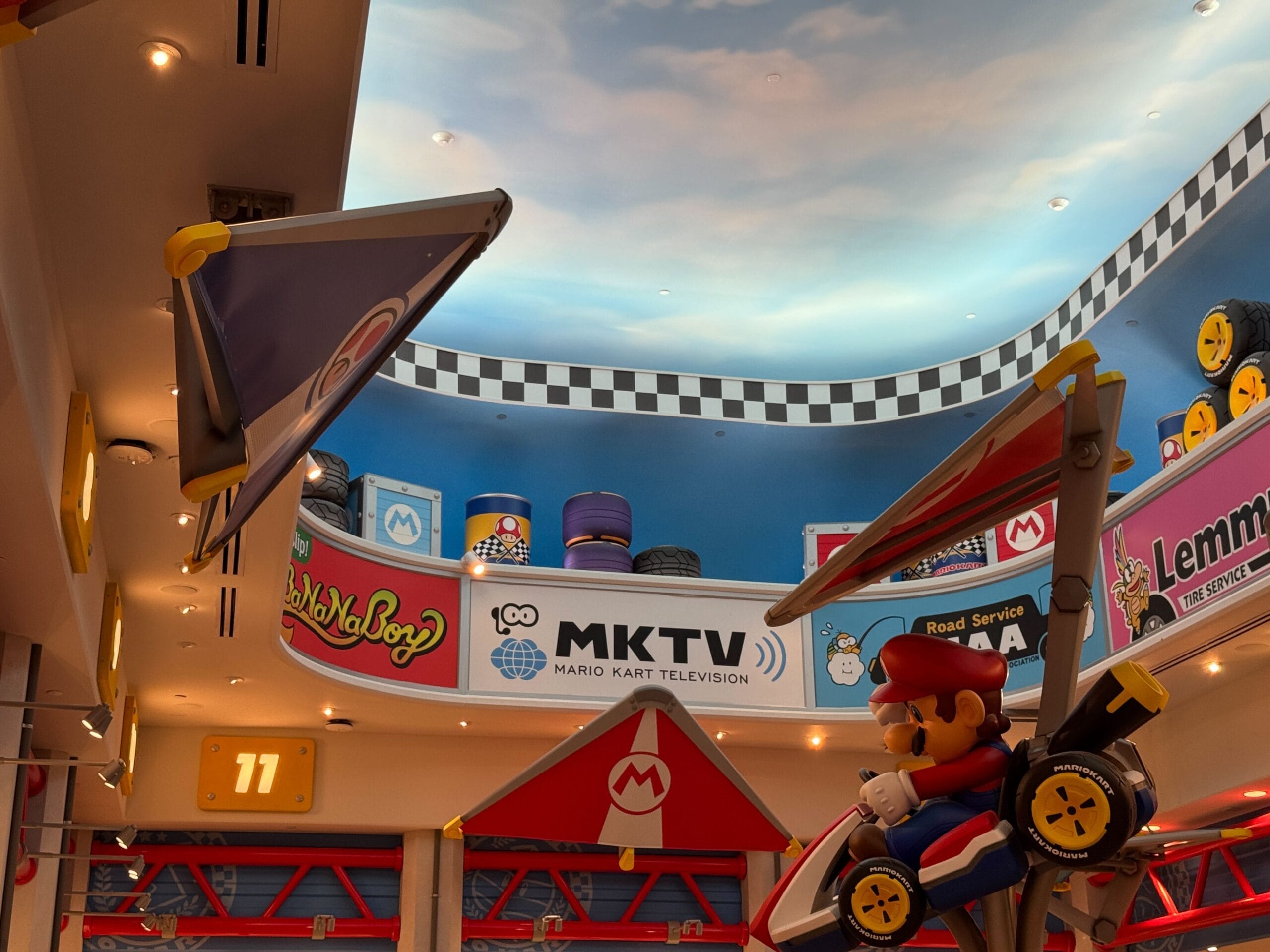 Indoor Mario Kart area with Mario Motors signs and sky ceiling, similar to immersive lands at Disney parks, but no Disney castle present.
