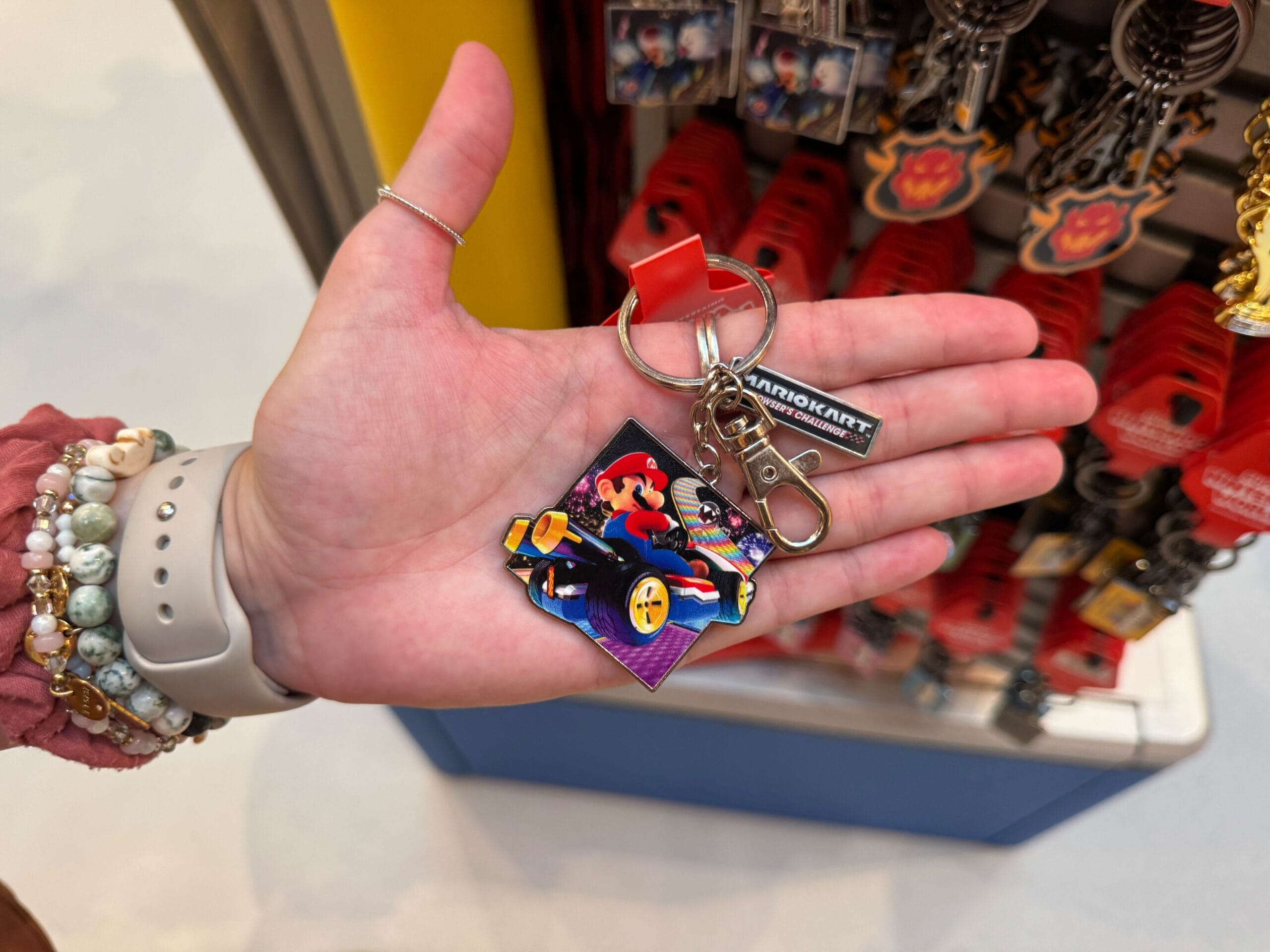 A hand holds a Mario Motors keychain in a store, with other colorful merchandise behind—no Disney castle sightings in view.