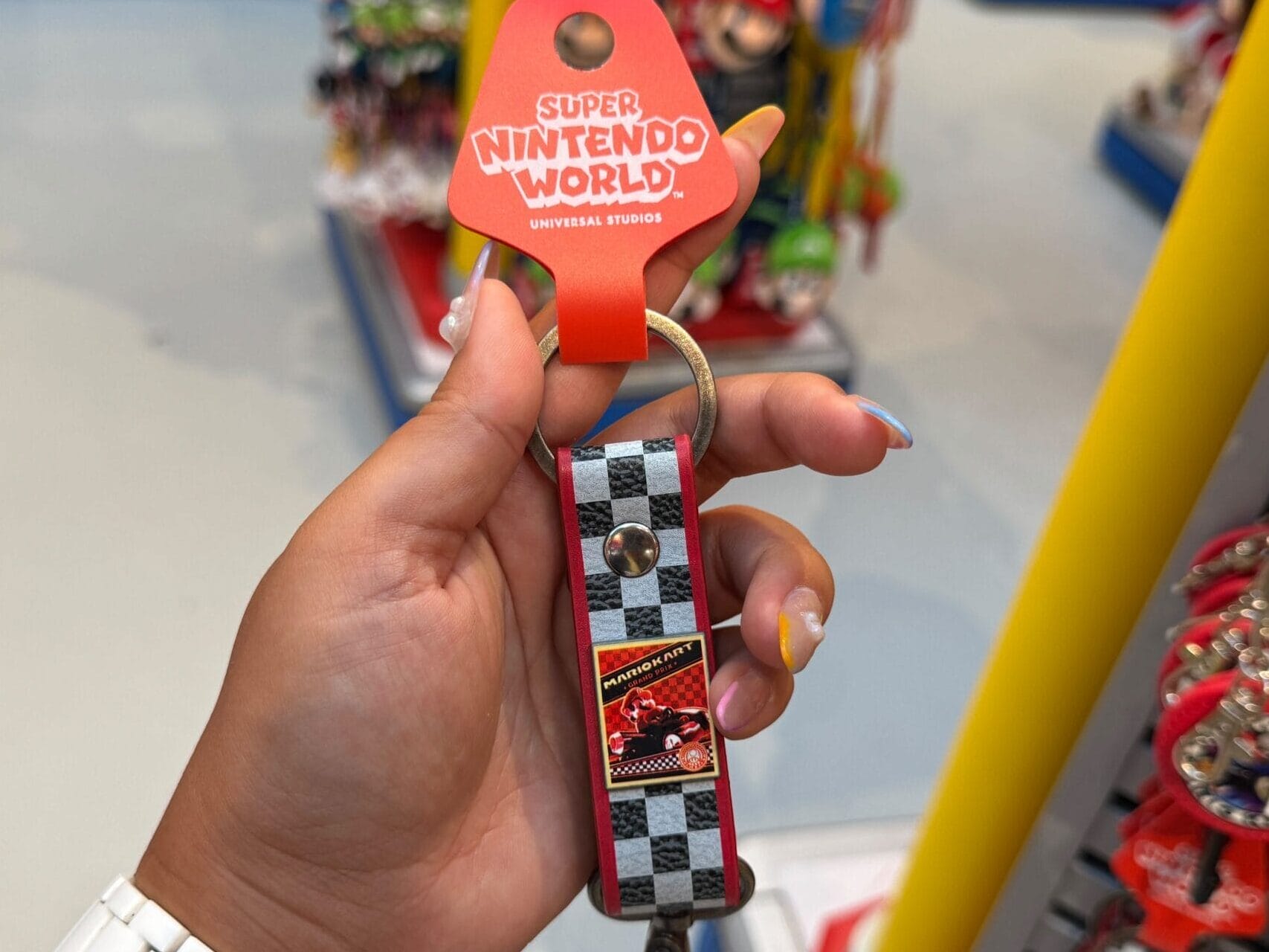 A hand holds Super Nintendo World Mario Motors merchandise in a vibrant shop at Epic Universe, not far from Disney’s iconic castles.