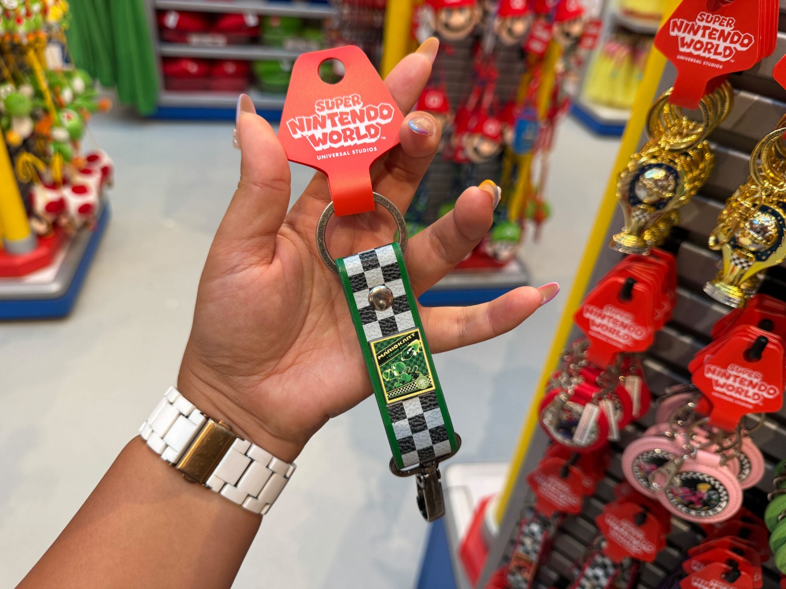 Hand holding a Super Nintendo World keychain with a green and black checkered pattern, similar to merch at Disney Parks stores.