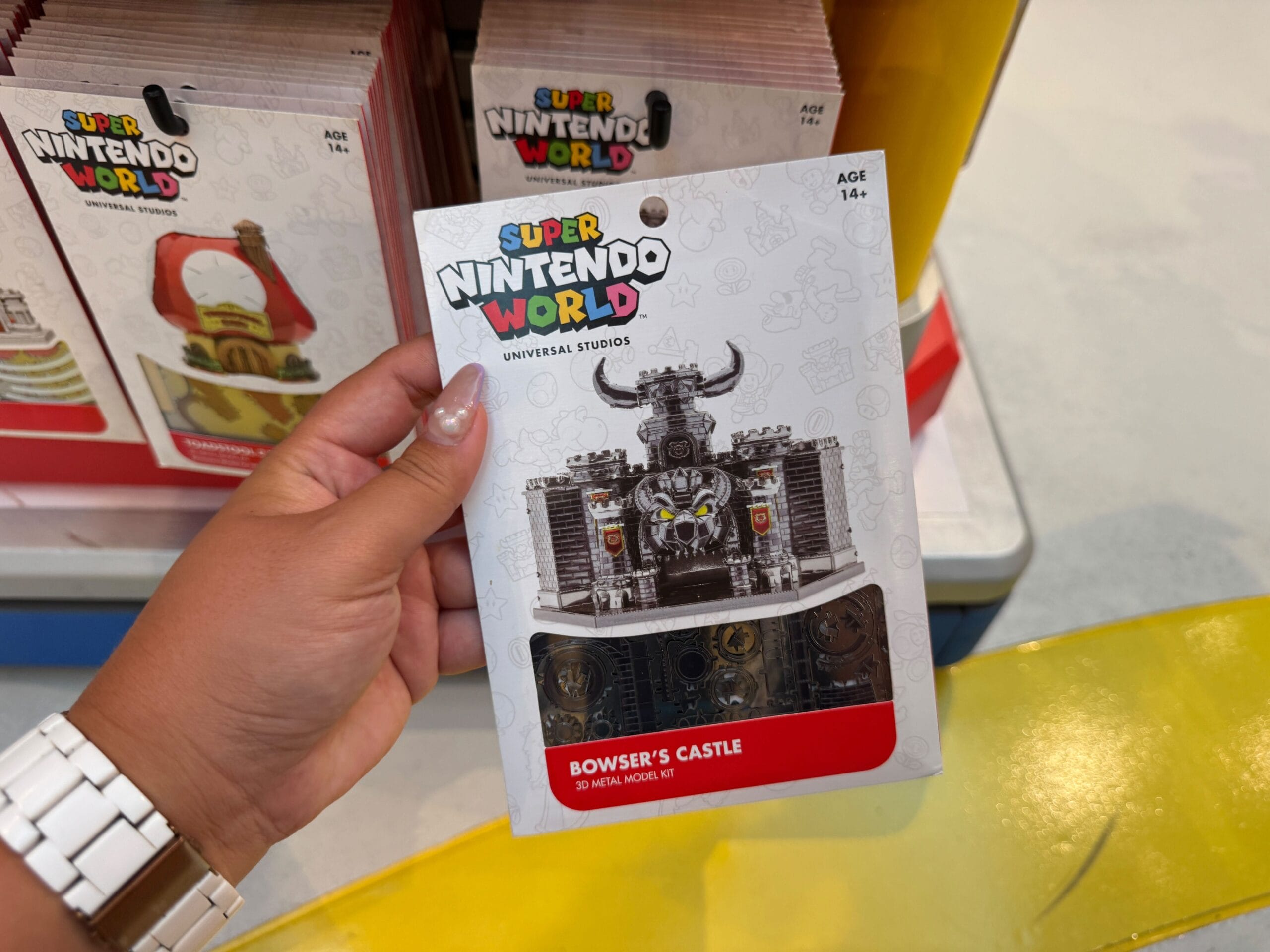 A hand displays Mario Motors Bowser’s Castle metal model kit—its spiky towers more menacing than any Disney castle—in a shop.
