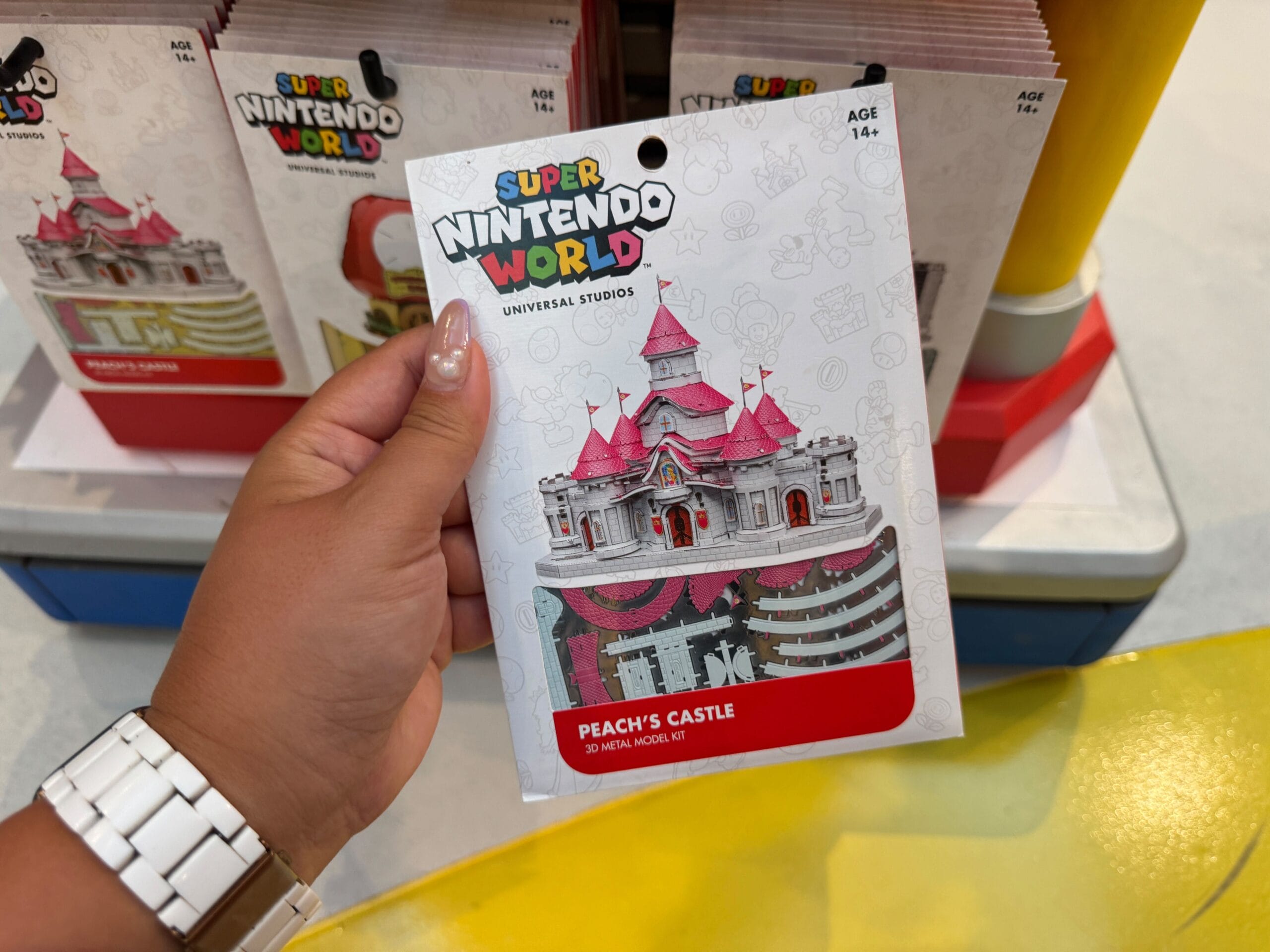 A hand holds a Peach’s Castle 3D model kit, its spires reminiscent of Disney castles but uniquely Super Nintendo World in style.