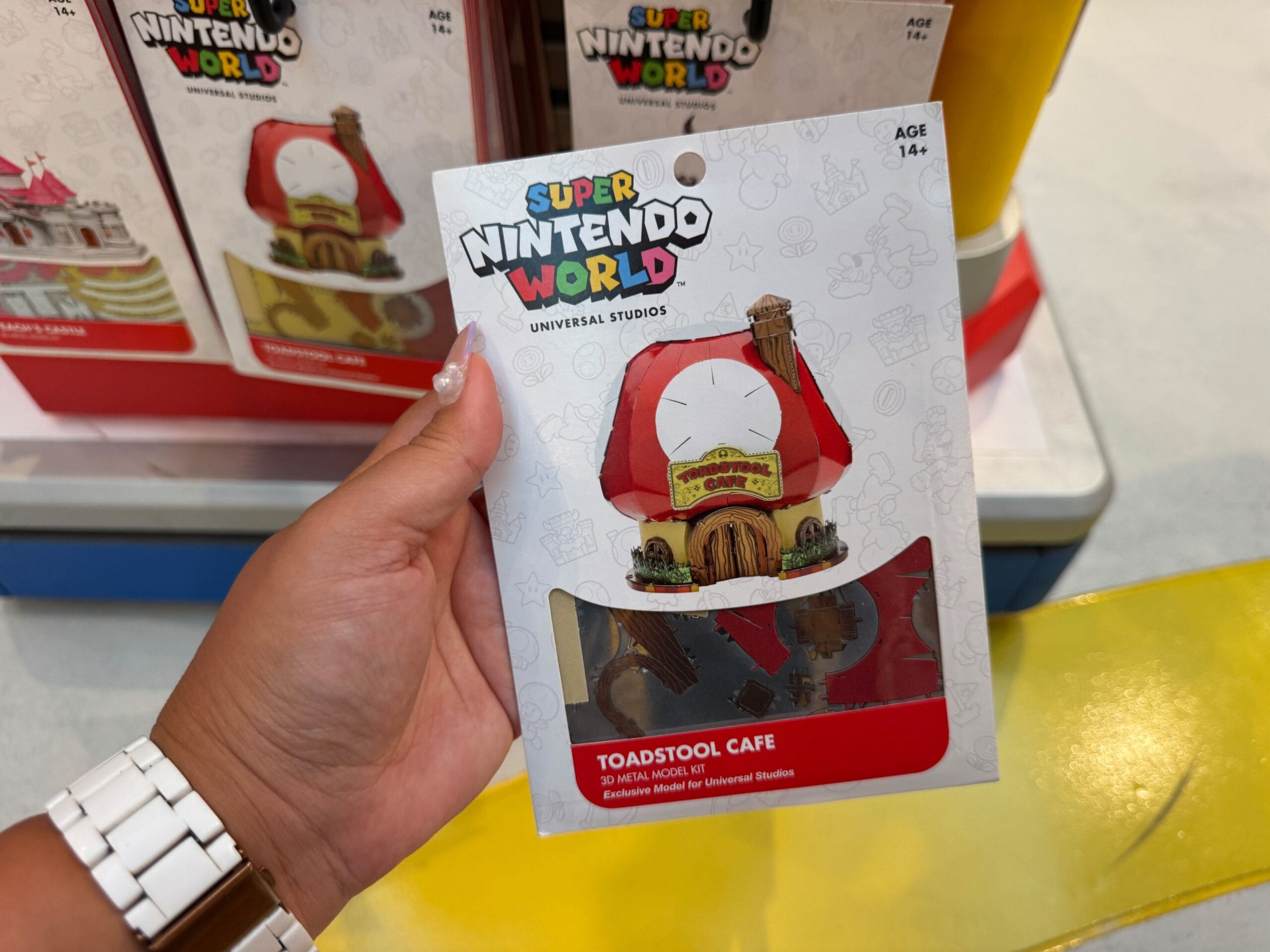 Hand holding a Super Nintendo World Toadstool Cafe model kit at Epic Universe, shelves behind—no Disney castle here to compare.