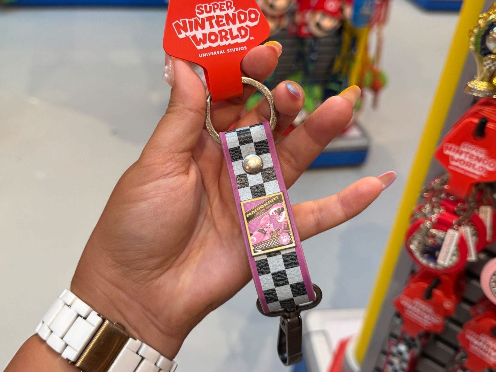 A hand holds a Yoshi keychain with a checkered design amid Mario Motors merch, a vibe similar to themed shops near Disney castles.