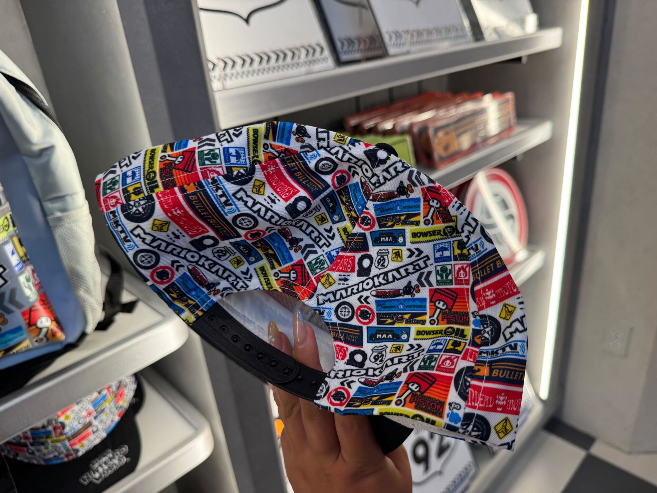 A hand holds a vibrant Mario Motors racing cap at a Super Nintendo World store—no Disney castle merch like at Magic Kingdom’s Emporium.