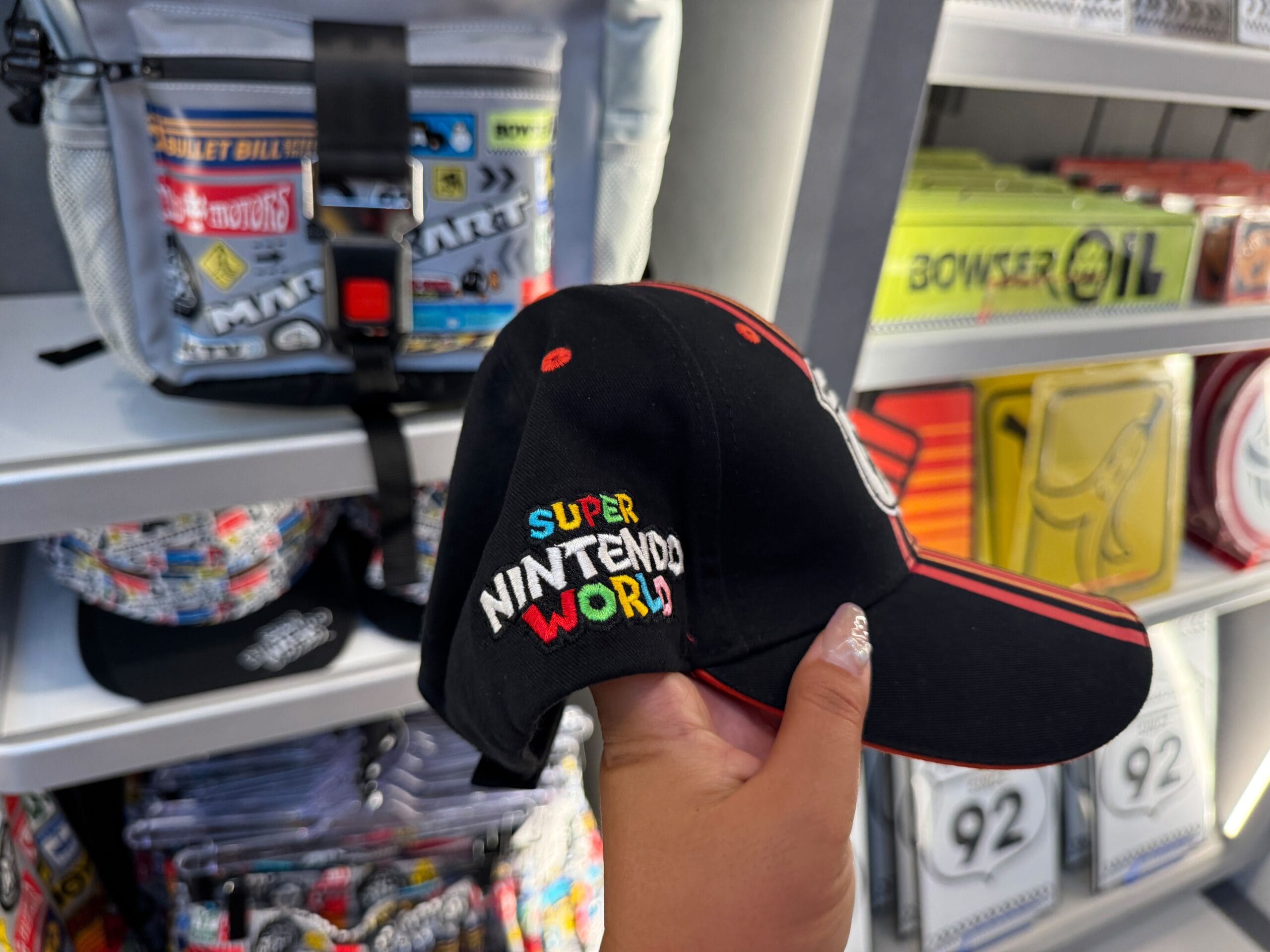 Hand holding a black Super Nintendo World cap in a theme park shop; background lacks Disney castle motifs or merch.