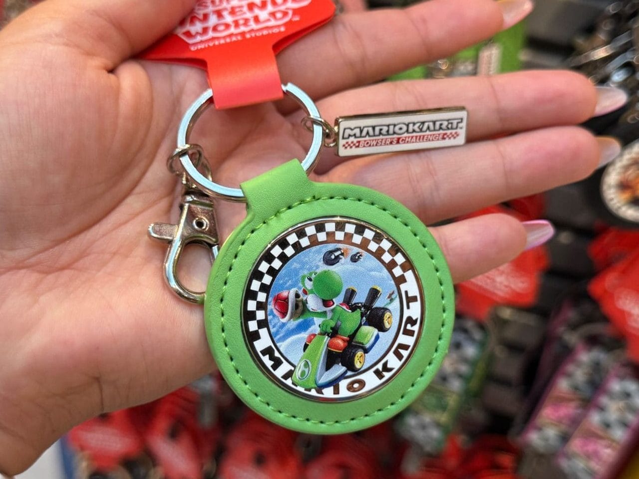 A hand holds a green Mario Kart Yoshi keychain, surrounded by Epic Universe Super Nintendo World souvenirs—no Disney castles in sight.