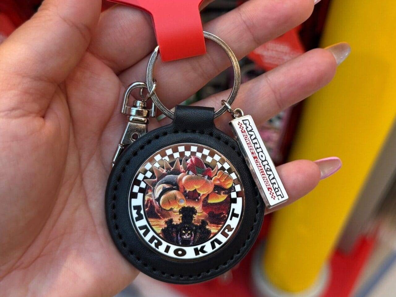 Hand holding a Mario Motors keychain with Super Nintendo World tag, similar to unique merchandise at Disney parks but not featuring any castle comparison.
