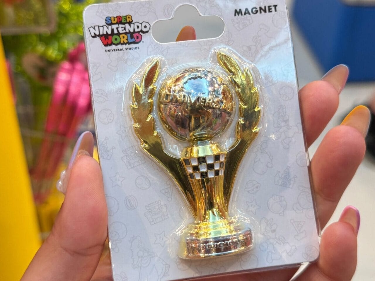 A hand holds a gold Mario Kart trophy magnet, similar to unique merch found near Cinderella Castle at Walt Disney World.