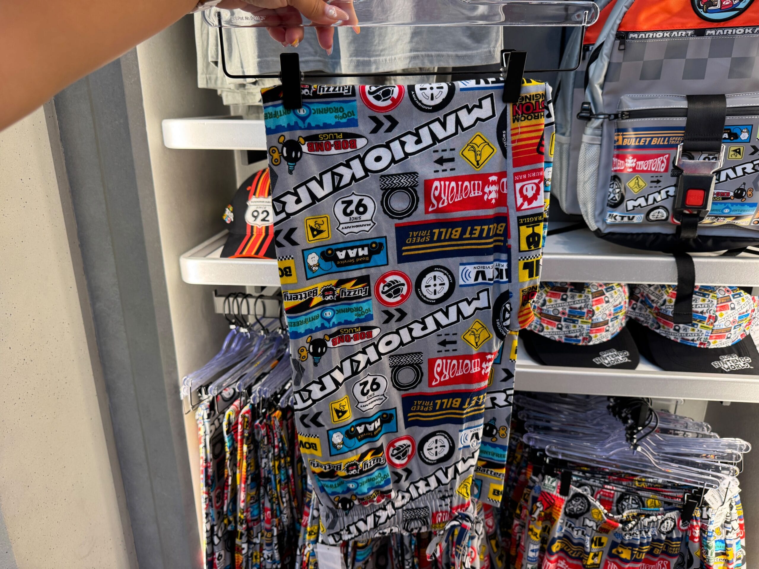 Hand holds colorful Mario Kart shorts with patches—fun themed gear like unique Disney Park clothing, but featuring Nintendo style.