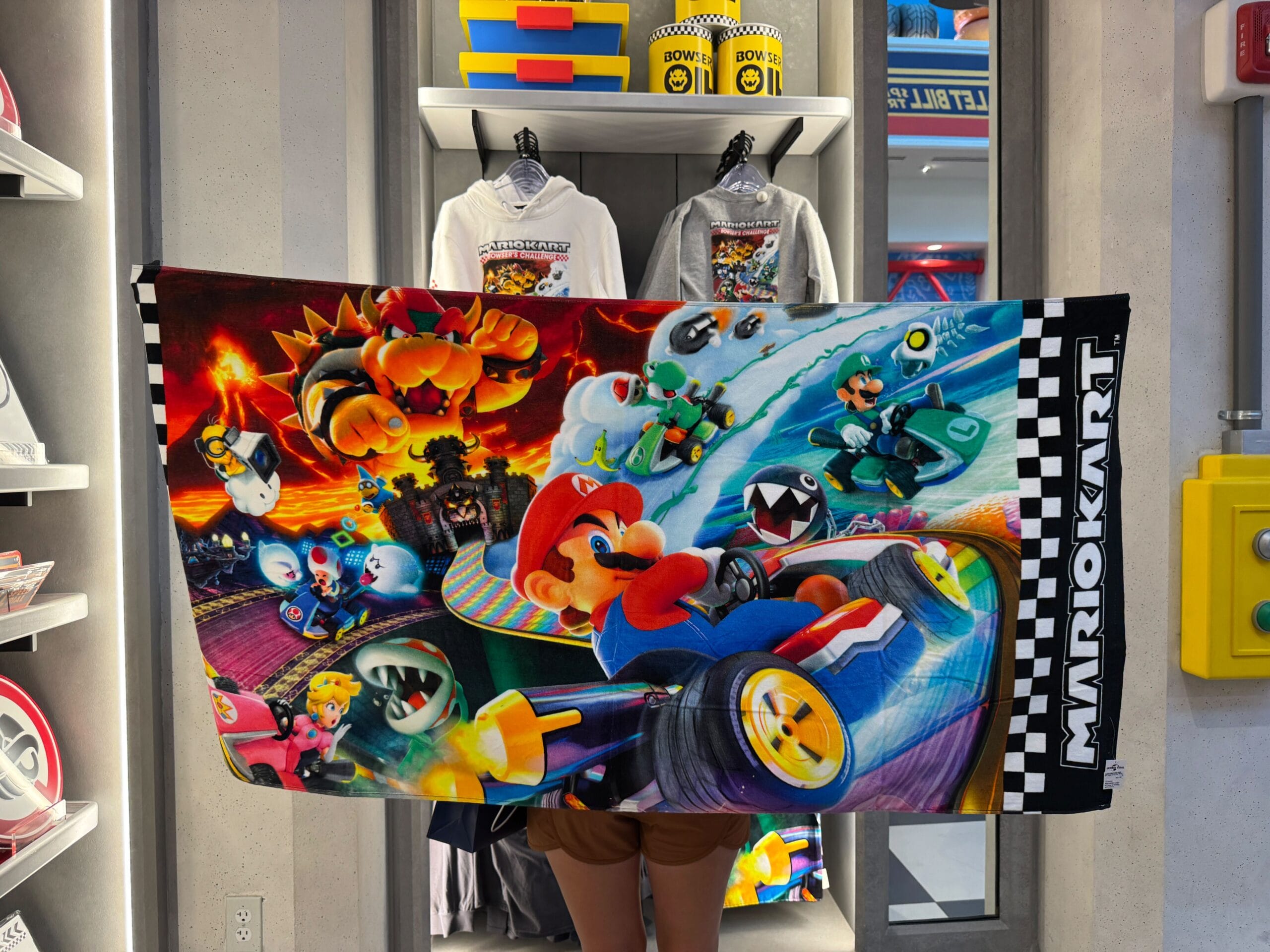 A person holds a colorful Mario Kart towel in a shop filled with Super Nintendo World items—definitely not your typical Disney castle merch.