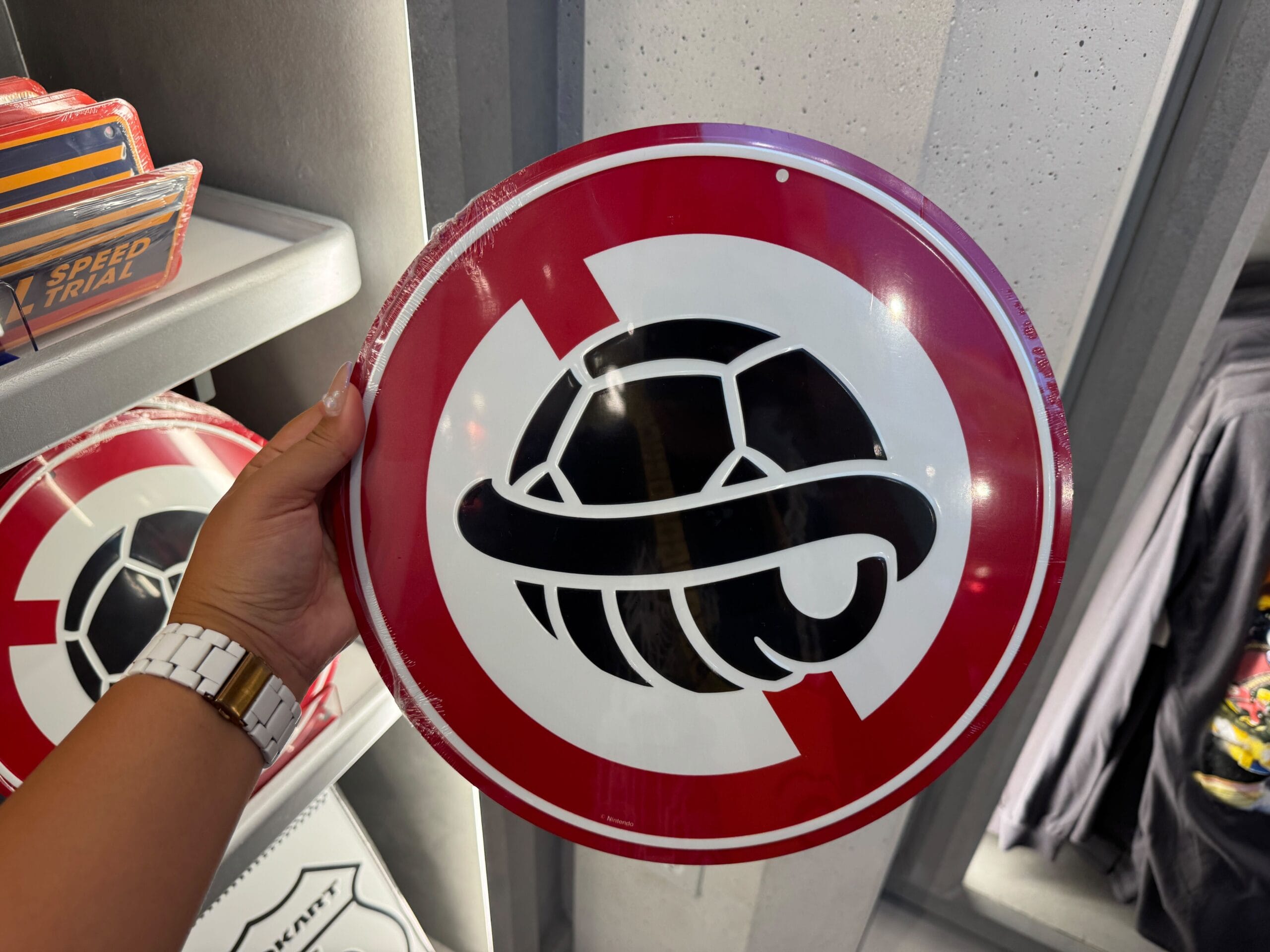 A hand holds a red and white Super Nintendo World sign with a crossed-out black turtle shell, unlike any Disney park signage.