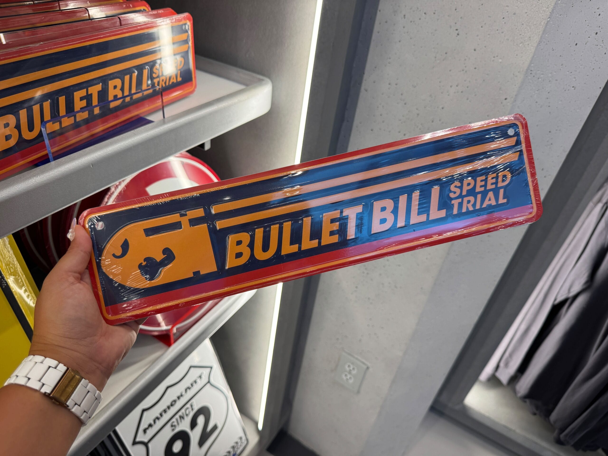 A hand displays a “Bullet Bill Speed Trial” sign from Epic Universe Mario Motors, merchandise on a shelf—not Disney park merch or seen near any castle like those in Disney World or Disneyland.