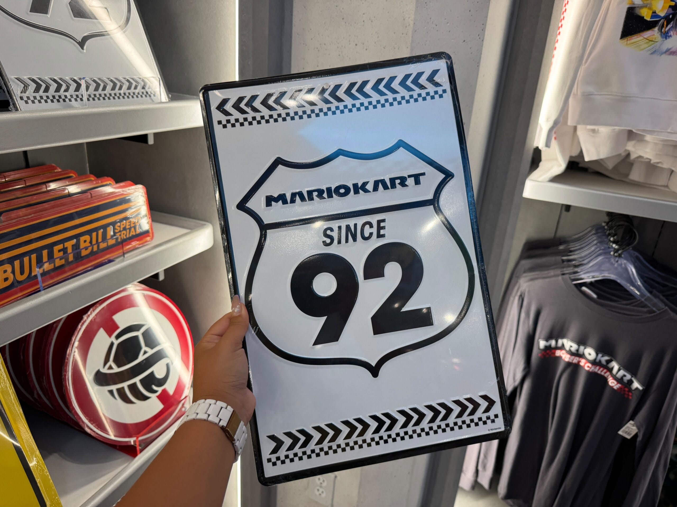 A person holds a Mario Kart sign among Mario Motors merchandise at Epic Universe, not far from Universal’s take on castle displays—distinct from any Disney castle like Cinderella Castle at Magic Kingdom or Sleeping Beauty Castle in Disneyland.