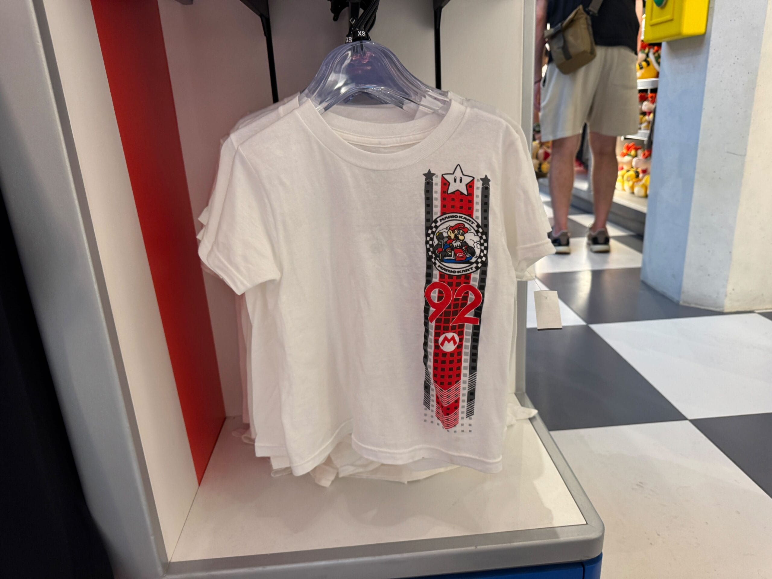 White t-shirt with a vertical Super Mario and 92 design, similar to themed park tees but not featuring Disney Park castles or icons.