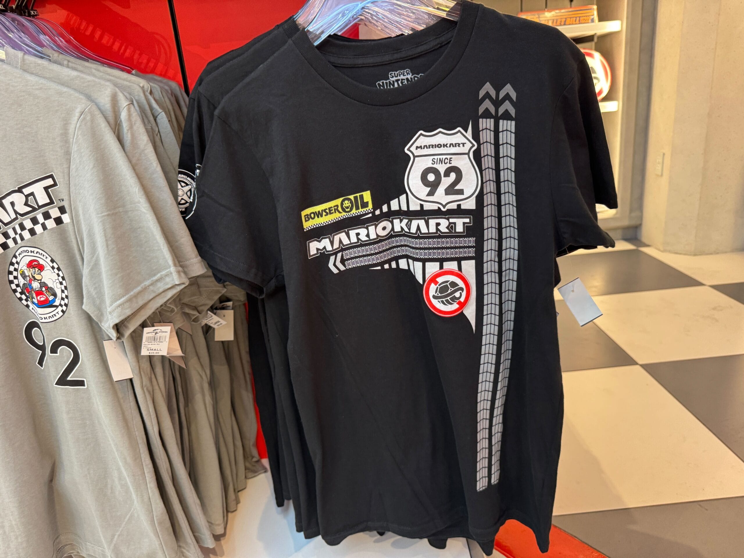Black Mario Kart tee with racing icons, "92" badge, Bowser Oil logo—Epic Universe Mario Motors merch, not Disney castle related.
