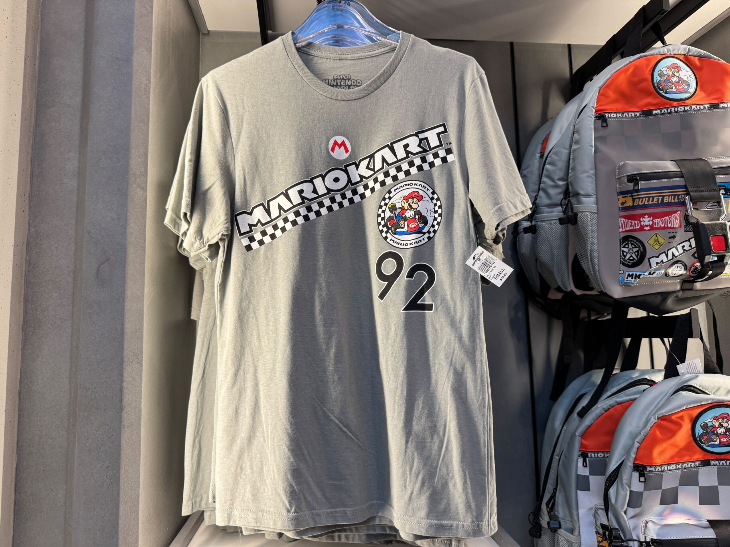 Gray Mario Kart t-shirt with Mario Motors logo, checkered stripe, and number 92 on a rack—no Disney castle motifs visible.