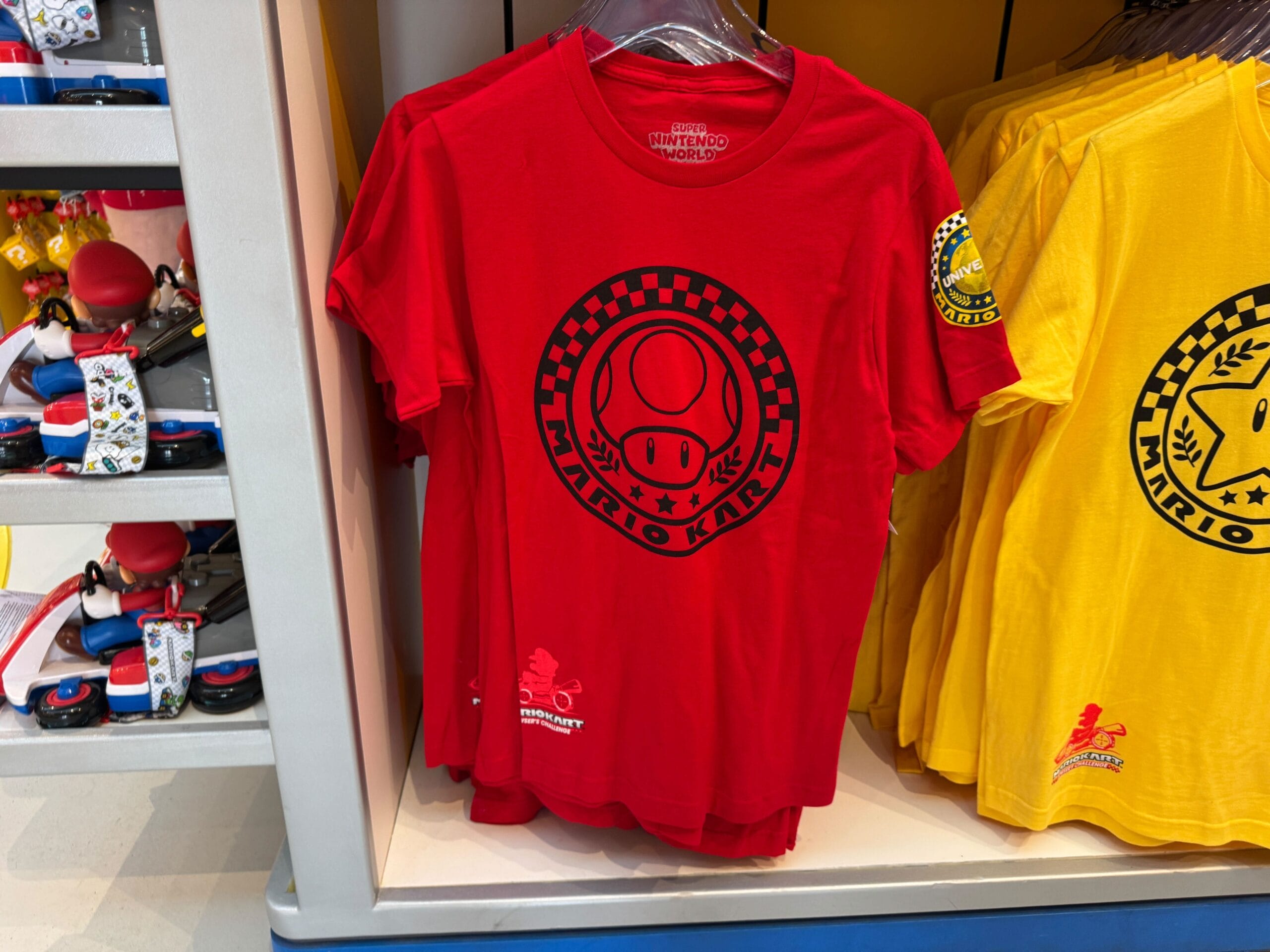 Red “Mario Kart” t-shirt with mushroom logo and checkered circle, similar to bold designs at Disney Parks but not featuring a castle.