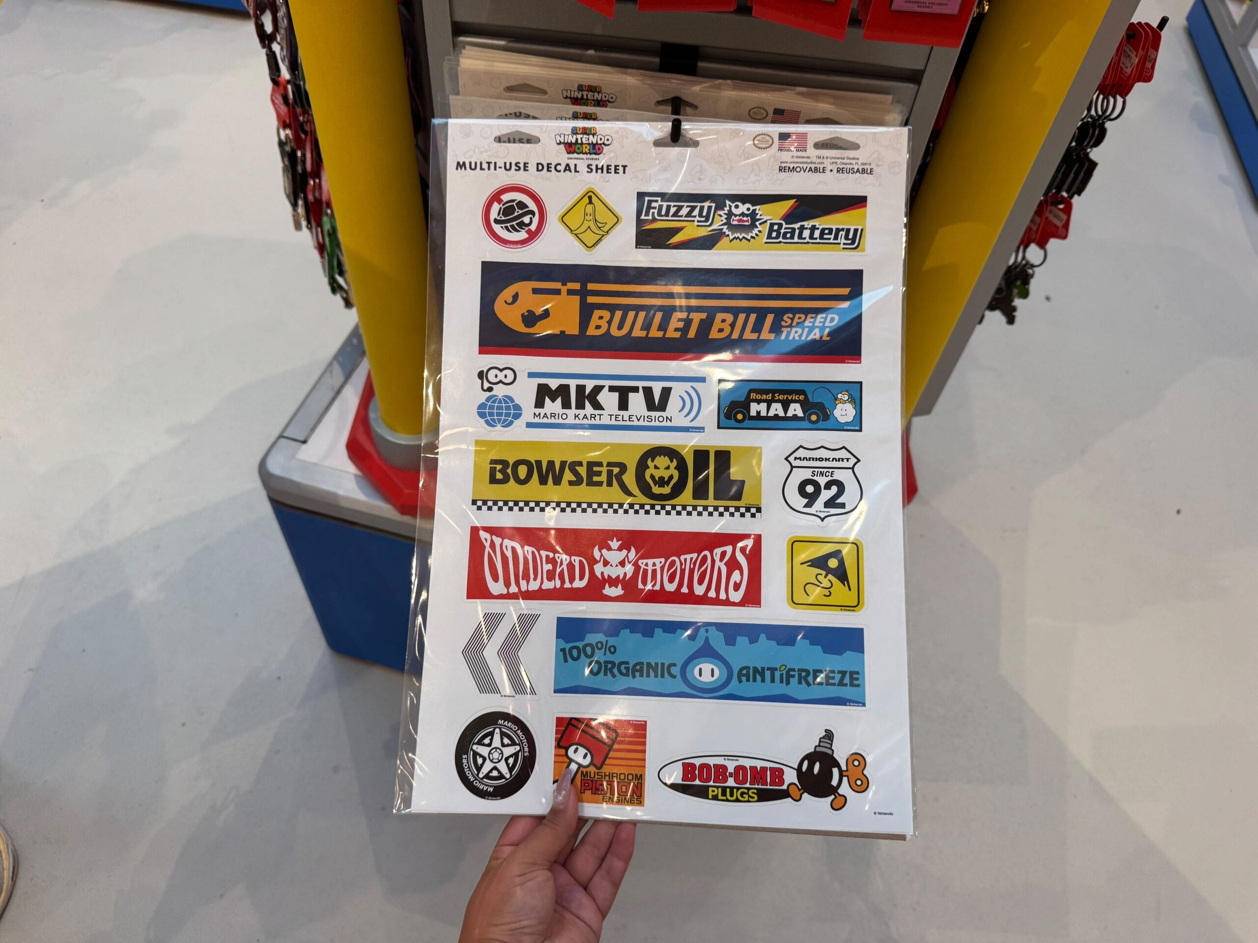 A hand holds a Mario Kart-themed sticker sheet from Super Nintendo World, reminiscent of the unique merch found in Disney Parks shops.