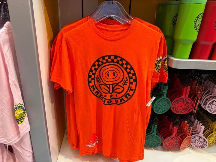 Bright orange Mario Kart tee with black logo, similar to theme park merch but found at Epic Universe, not a Disney park castle display.
