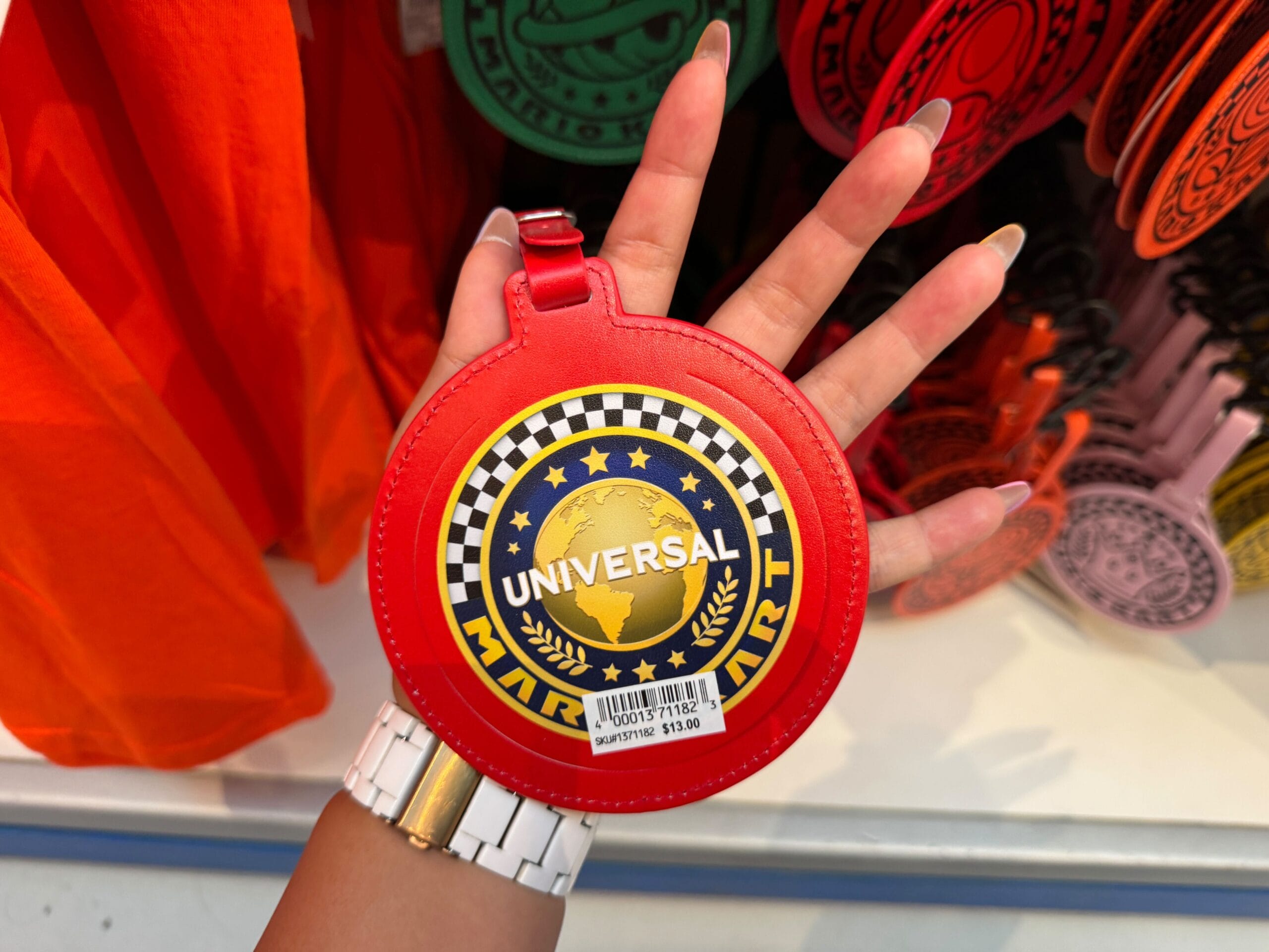 A hand displays a red Universal Studios luggage tag with a globe, reminiscent of unique theme park merch unlike any Disney castle souvenir.
