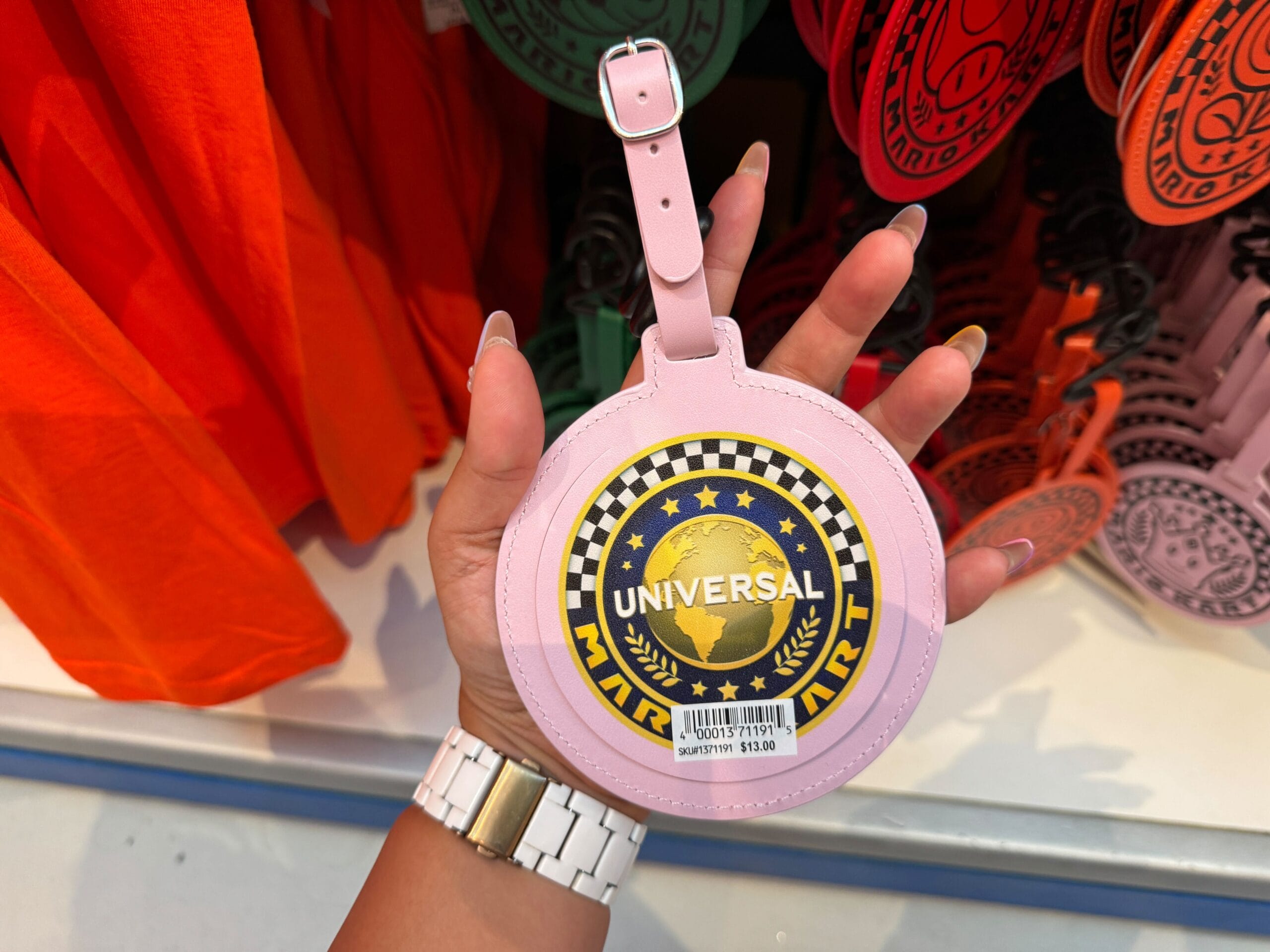 Hand holding a pink round Universal Studios Super Nintendo luggage tag, $13.00—unlike any Disney merch found near its fairytale castles.