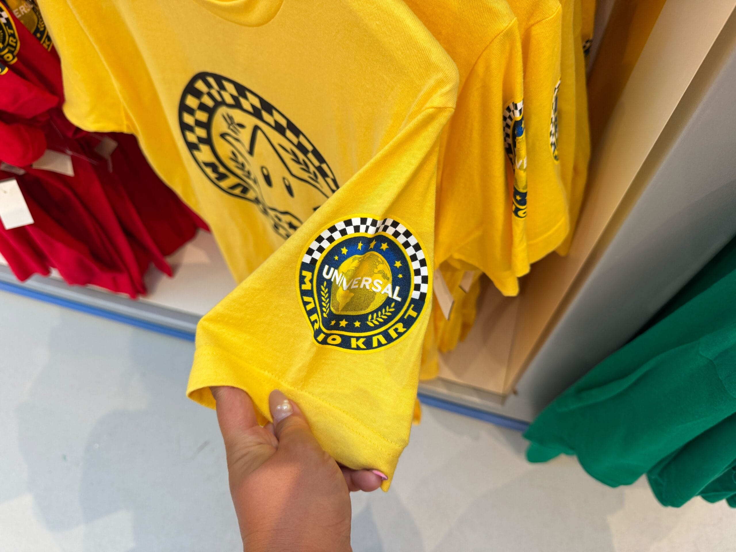 Hand holding a yellow Mario Kart shirt with "Universal" logo, similar to unique merch found at Disney parks, but from Epic Universe.
