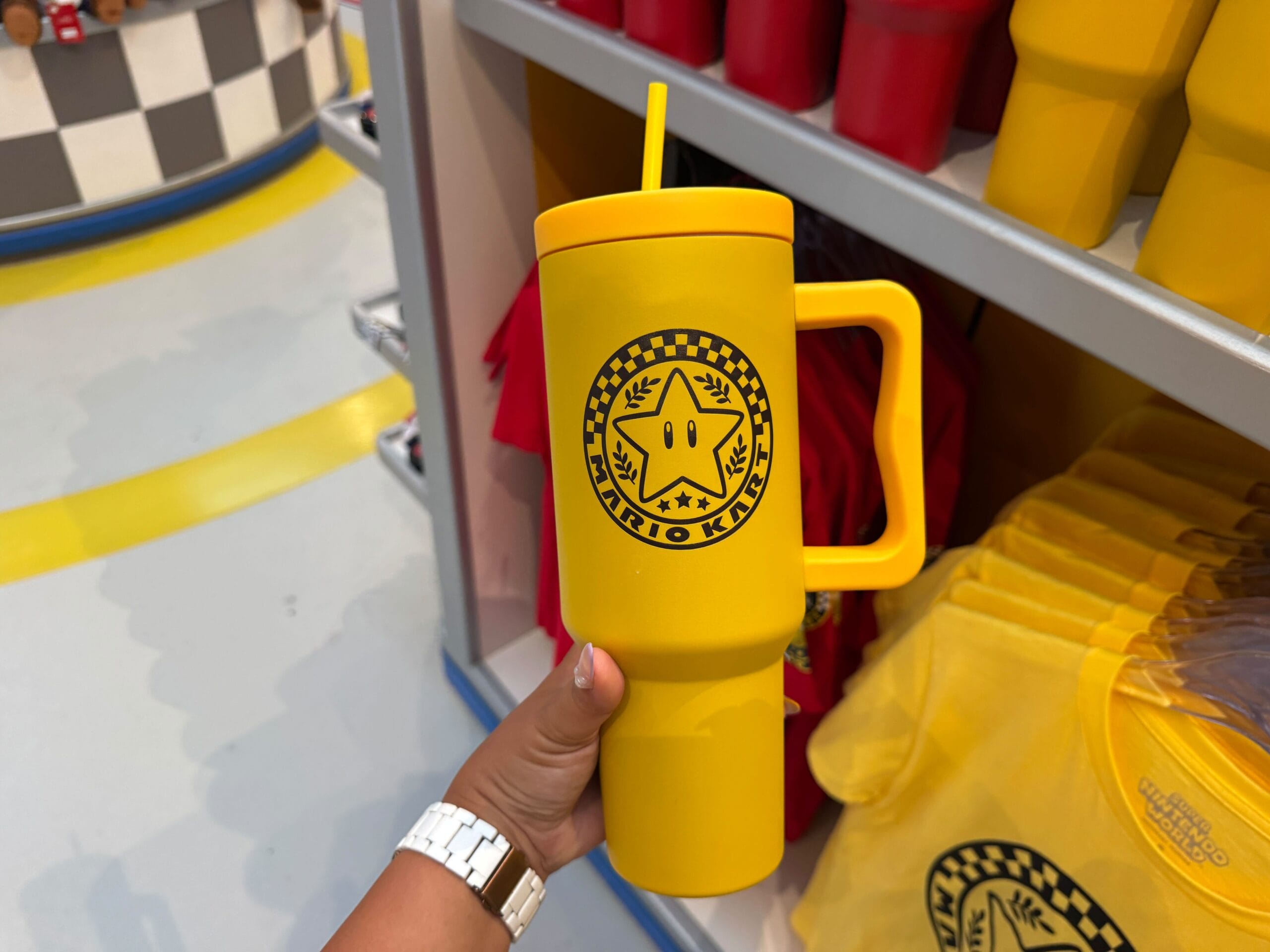 A hand holds a yellow Mario Kart cup with a star emblem—Mario Motors merch at Super Nintendo World, not seen in Disney parks.