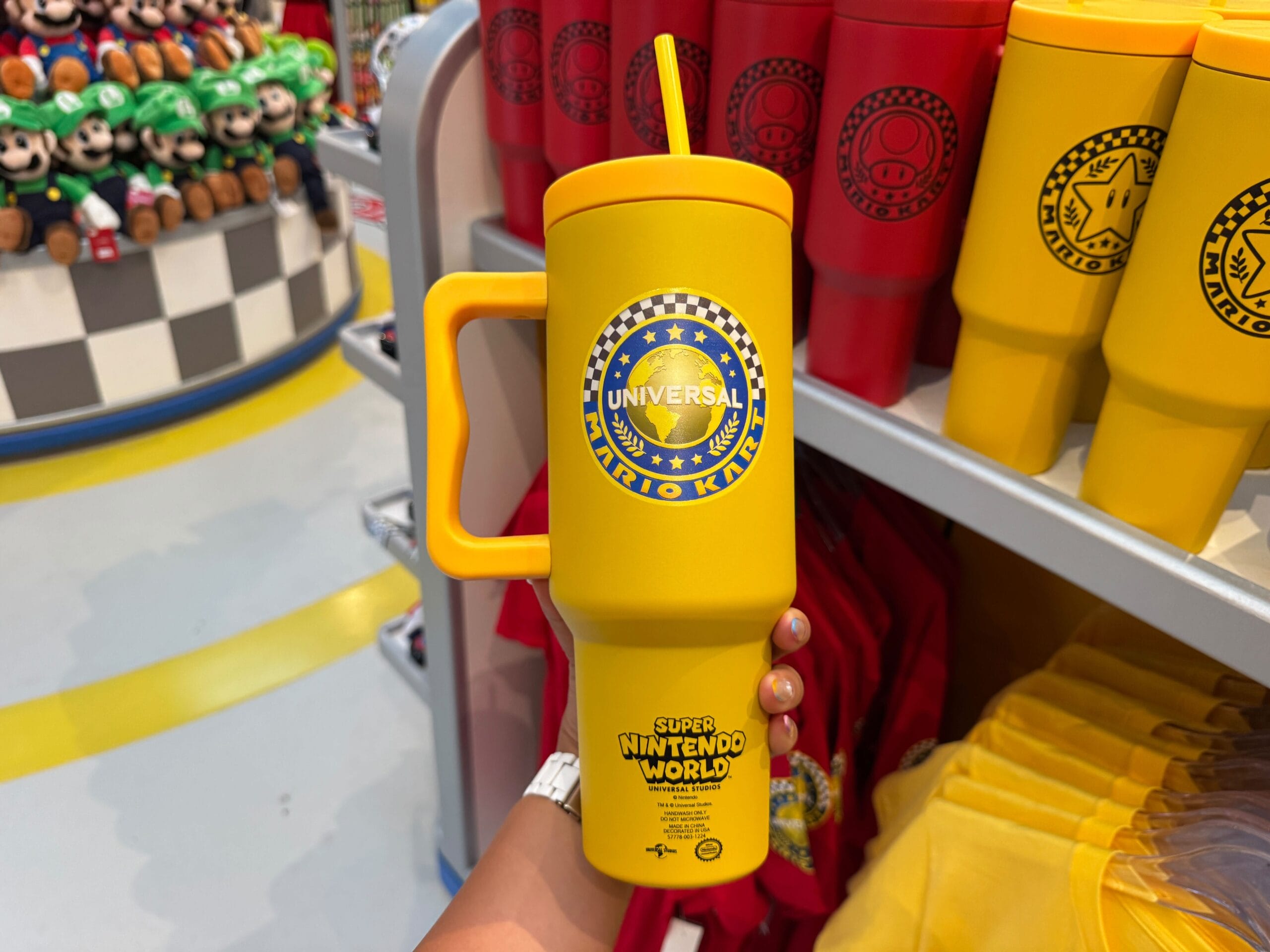 A hand holds a yellow Mario Motors mug in a shop with bright Super Nintendo World items, not unlike Disney Parks merch stores.
