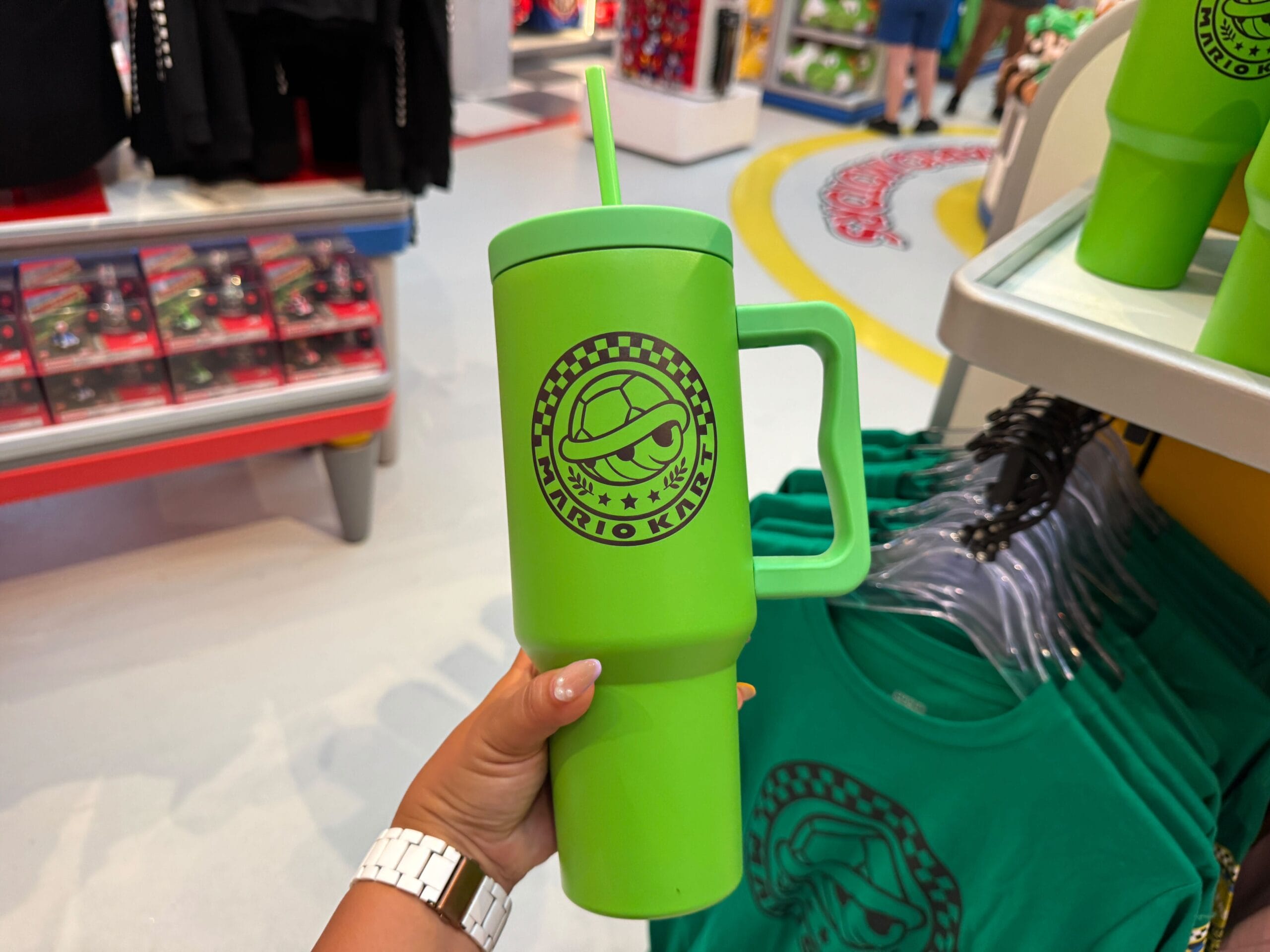 A hand holds a large green Mario Kart cup with a straw in a shop—much like themed sippers seen at Disneyland parks worldwide.