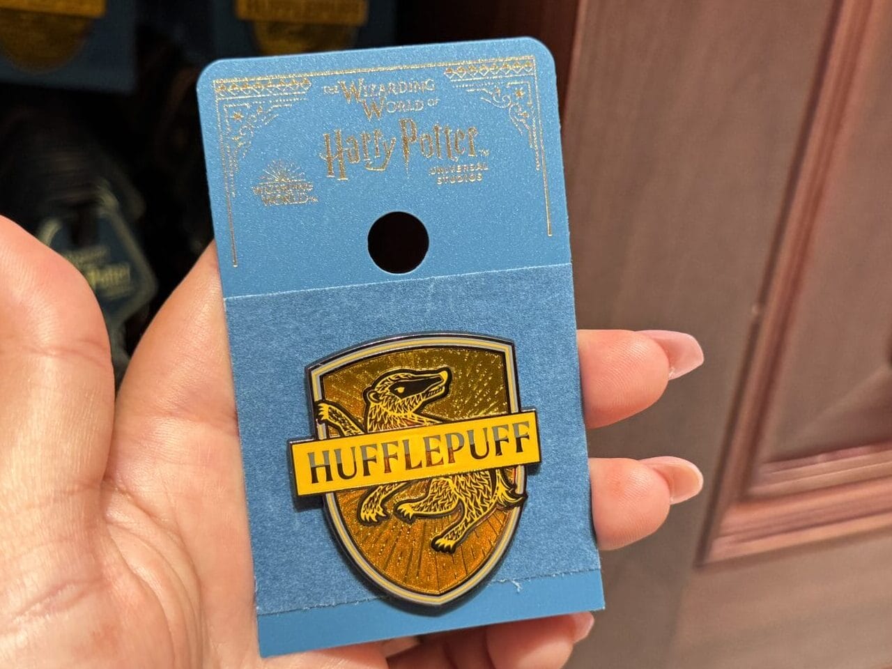 A hand holds a Hufflepuff crest pin, part of Wizarding World of Harry Potter merchandise at Epic Universe.