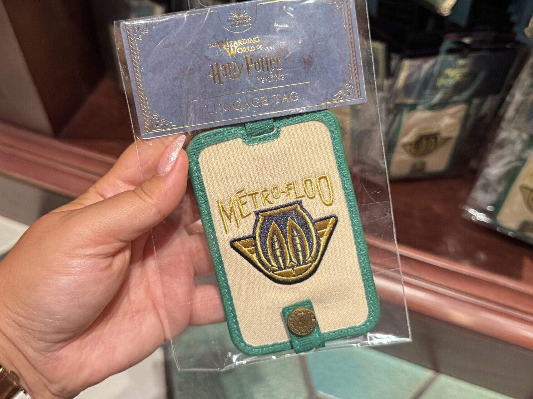 A hand holds a packaged "Metro-Floo" luggage tag, part of exclusive Wizarding World of Harry Potter merchandise on display.