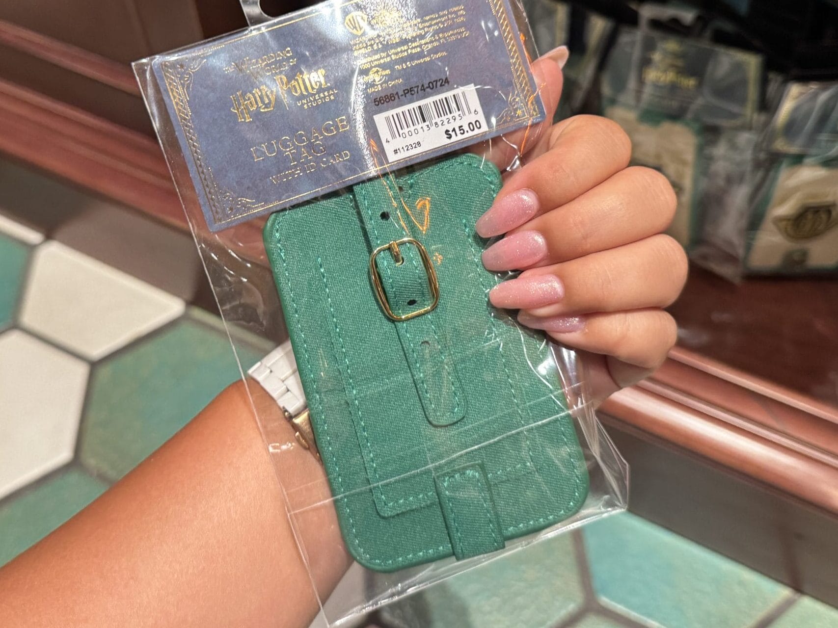 A hand holds Slytherin-themed Harry Potter merchandise at the Wizarding World of Harry Potter, with more tags in the background.