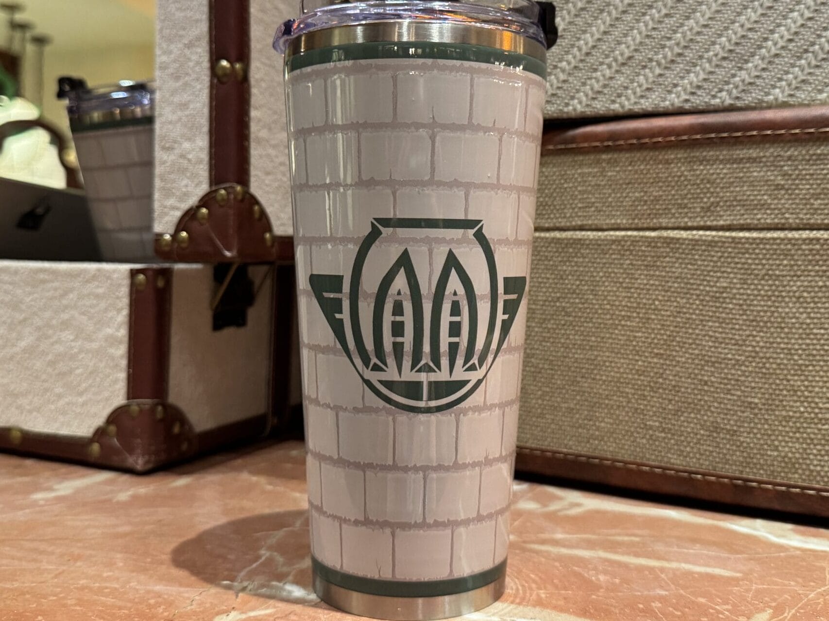A Wizarding World of Harry Potter merchandise travel tumbler rests on marble before vintage suitcases.
