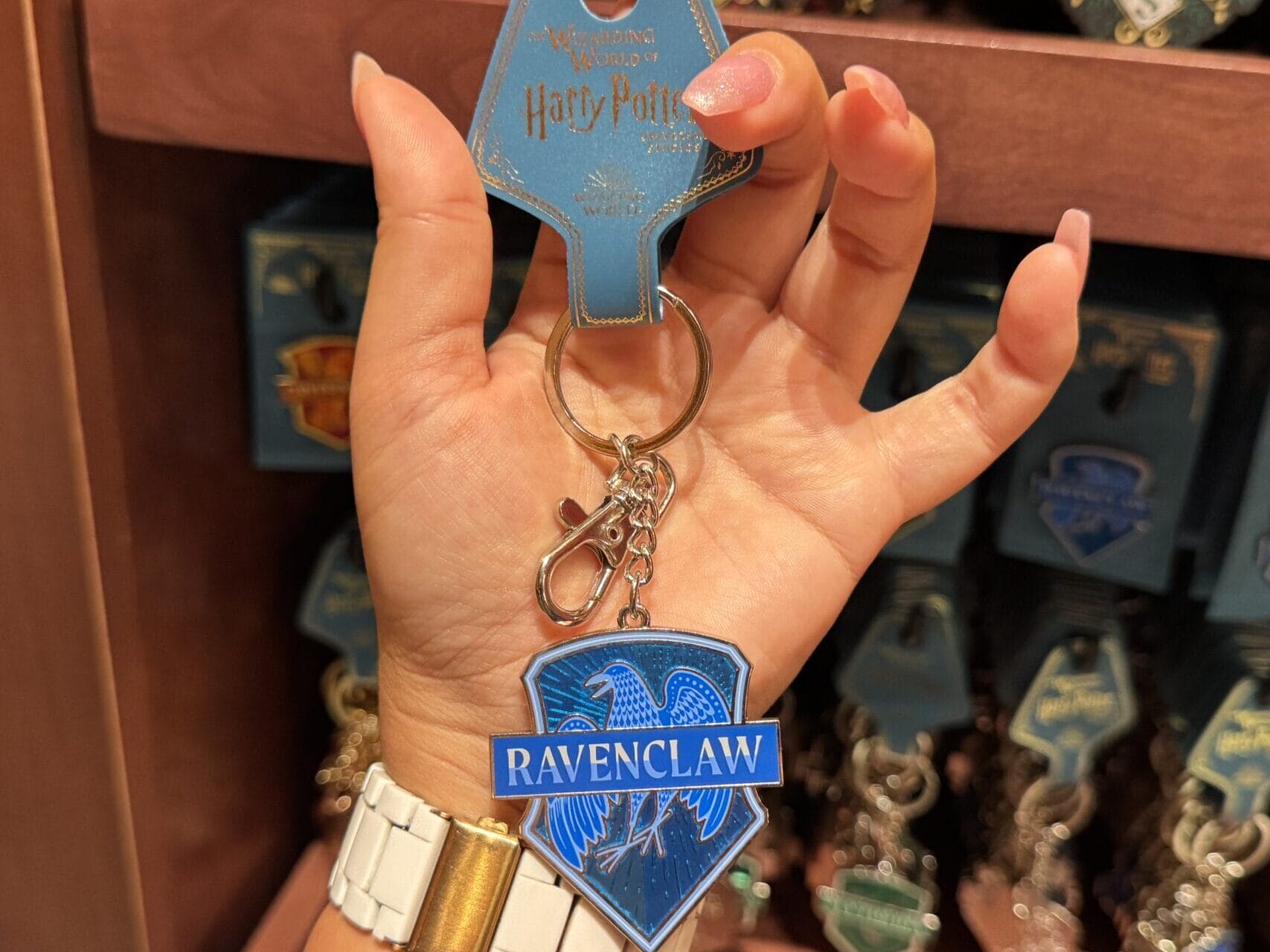 A hand holds a Harry Potter Ravenclaw keychain in-store, surrounded by Wizarding World of Harry Potter merchandise displays.