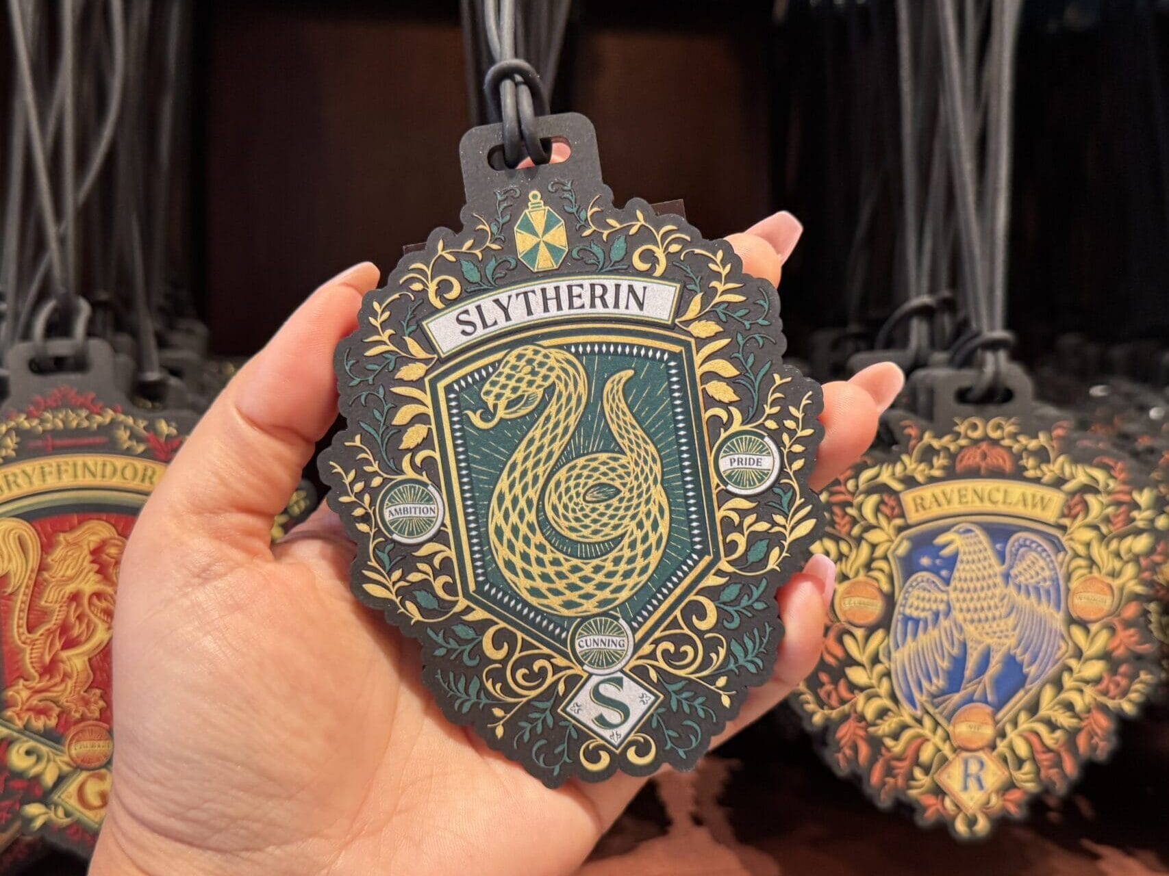 A hand holds a Slytherin ornament among Wizarding World of Harry Potter merchandise on display in a store.