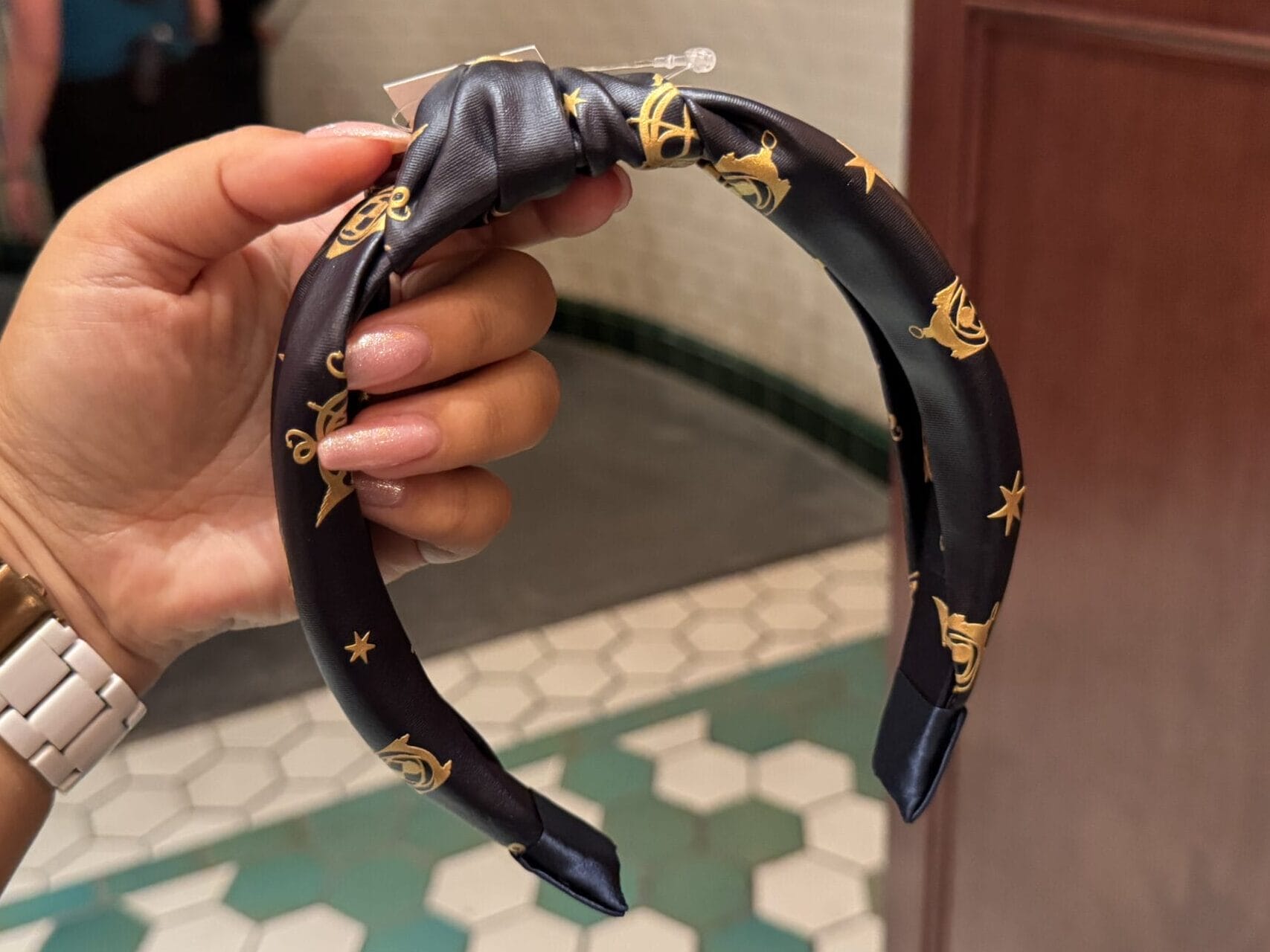 A hand holds a navy blue headband with gold designs—Wizarding World of Harry Potter merchandise—in a tiled room.