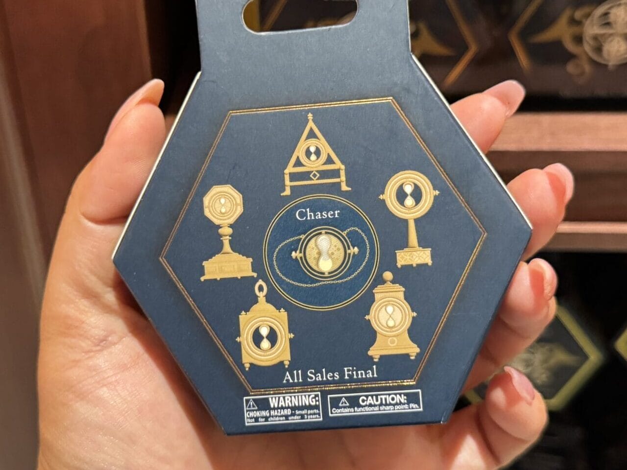 A hand holds a hexagonal box with gold symbols and "Chase" text—Wizarding World of Harry Potter merchandise on display.