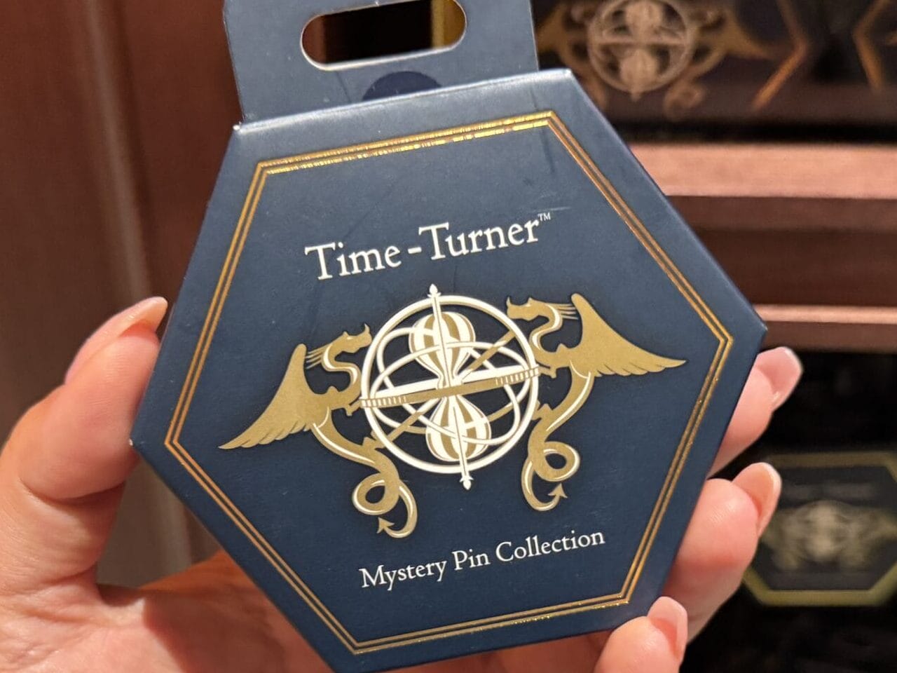 Hand holding a hexagonal "Time-Turner" Mystery Pin Collection box, exclusive Wizarding World merchandise on display.